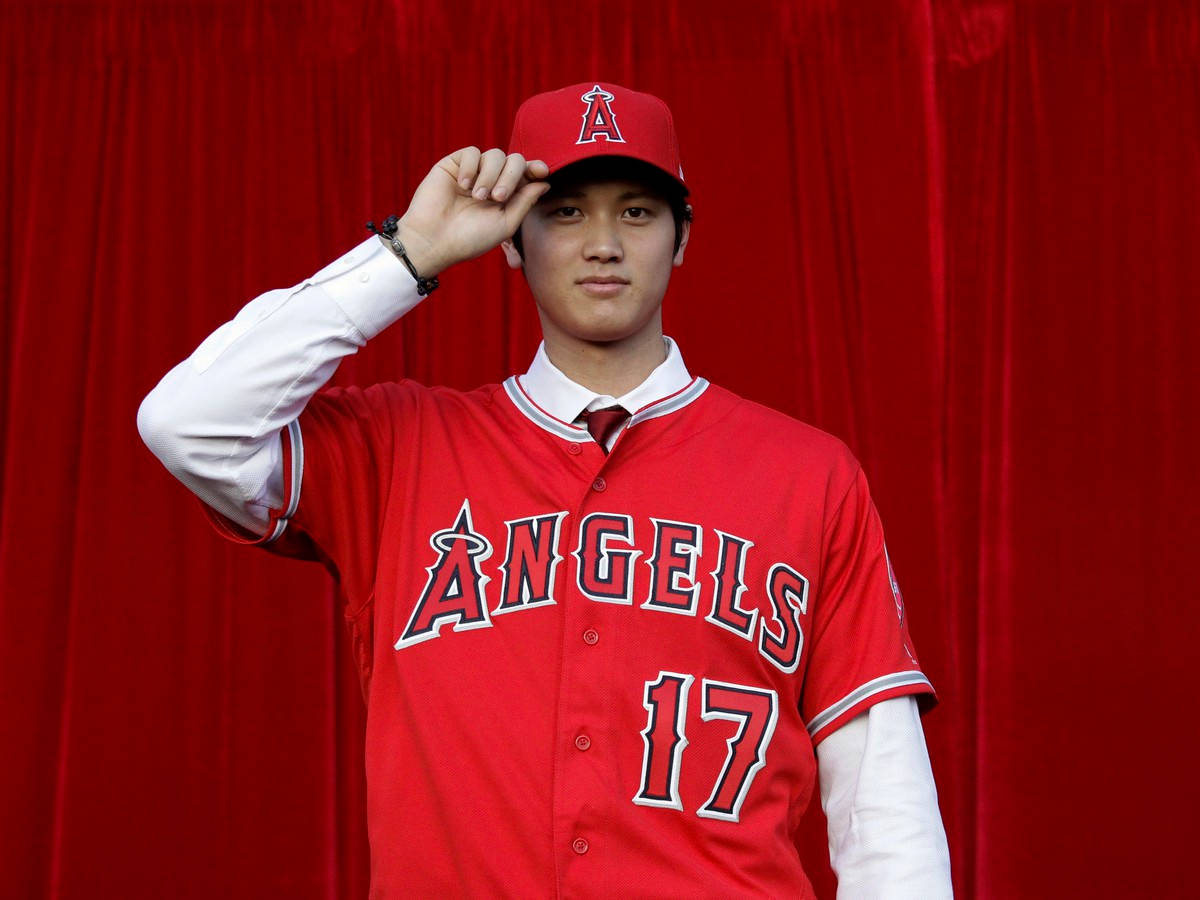 大谷翔平脫帽致意 壁紙 — 一位身穿紅色天使隊17號球衣的年輕棒球運動員，在濃郁的紅色窗簾背景下自信地敬禮。
