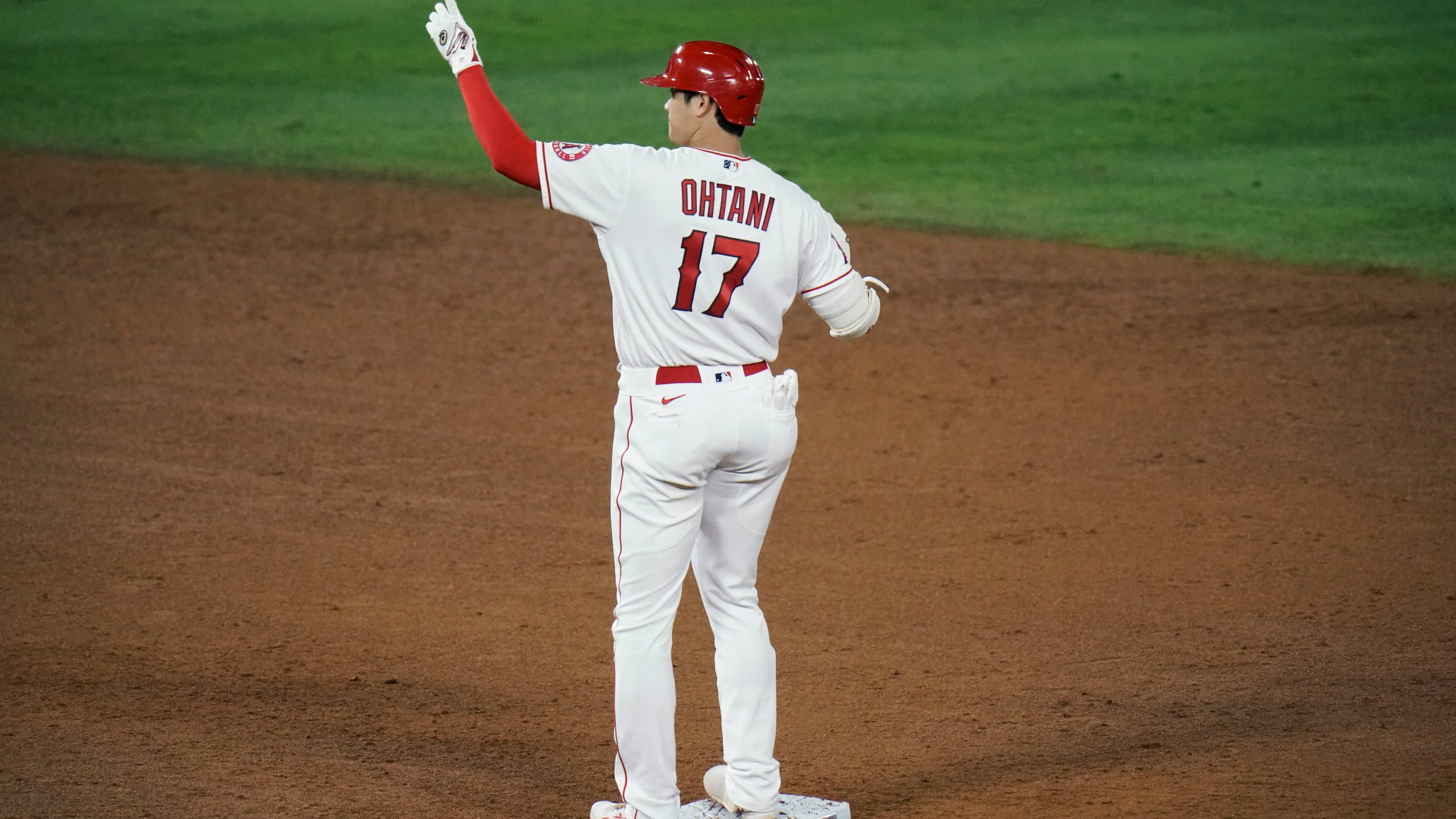 大谷翔平身穿17號球衣 壁紙 — 身穿白色球衣、紅色17號的棒球選手大谷翔平在球場燈光下，於內野紅土區的本壘板向觀眾揮手。