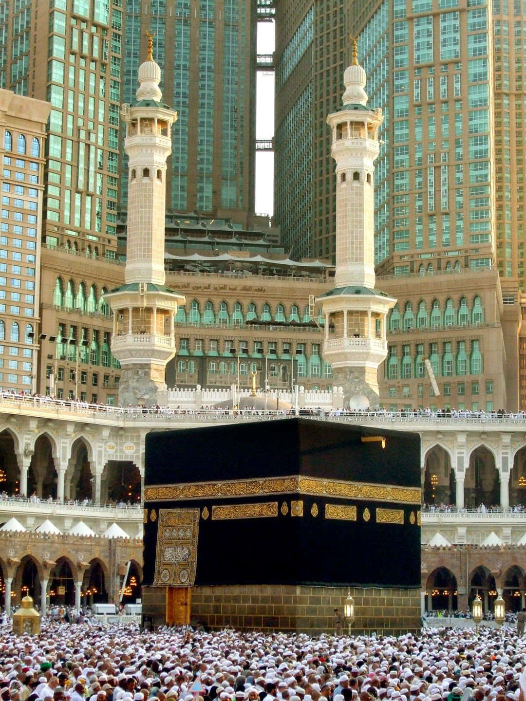 Makkah 桌布 壁紙 — 大量人群包圍著麥加黑色的卡巴天房，背景是高聳的現代摩天大樓。