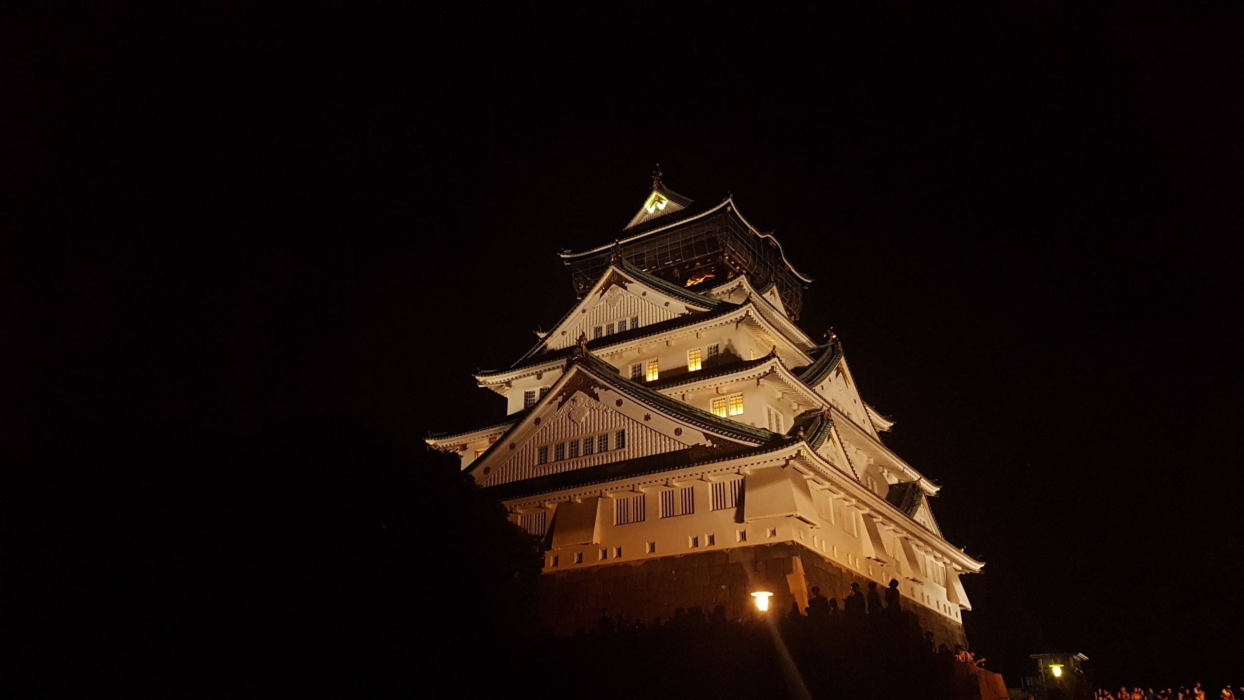 大阪城夜空 壁紙 — 一座雄偉的燈光照明日本城堡聳立在漆黑的夜空下，窗戶透出溫暖的光芒。