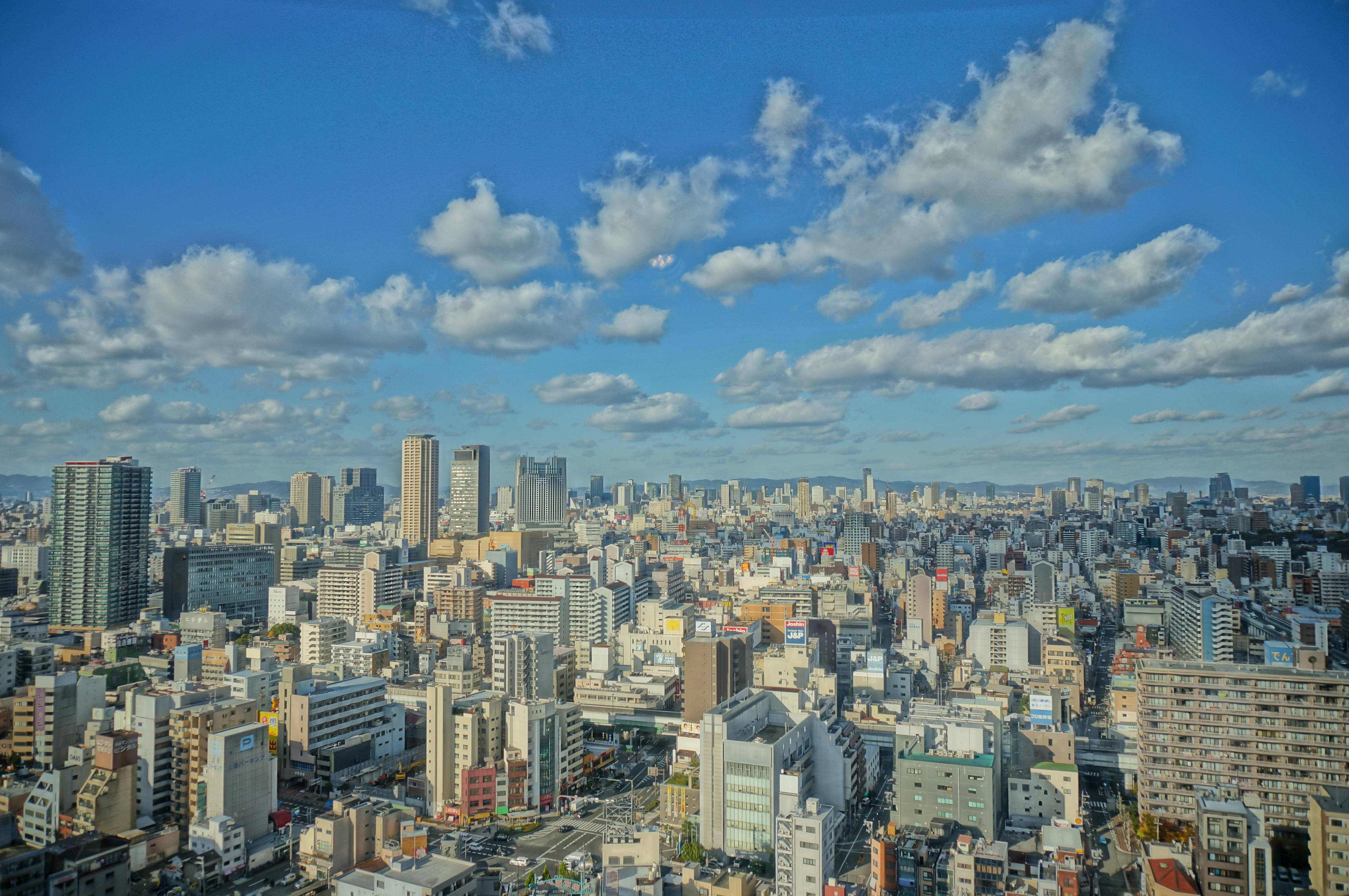 大阪城市全景 壁紙 — 在晴朗藍天與蓬鬆白雲點綴下，一片廣闊的城市天際線。