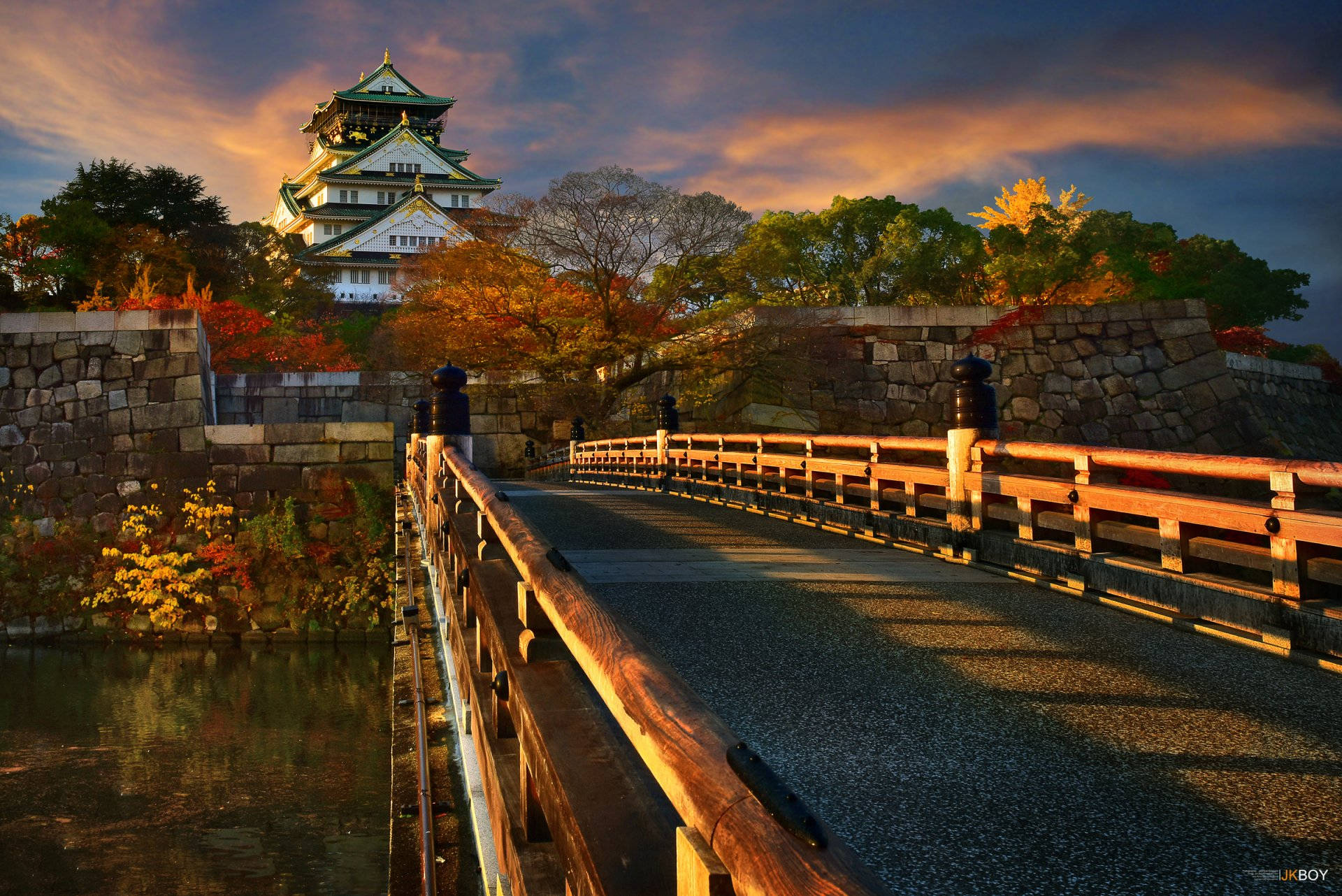 大阪城橋 壁紙 — 一條木橋通往一座雄偉的日本城堡，在充滿活力的日落天空下閃耀著秋葉。