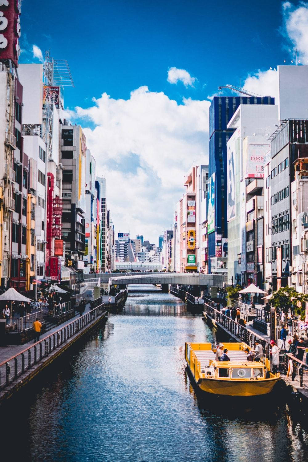 大阪娛樂區 壁紙 — 東京一條充滿活力的城市運河，一艘黃色觀光船在藍天白雲下航行。