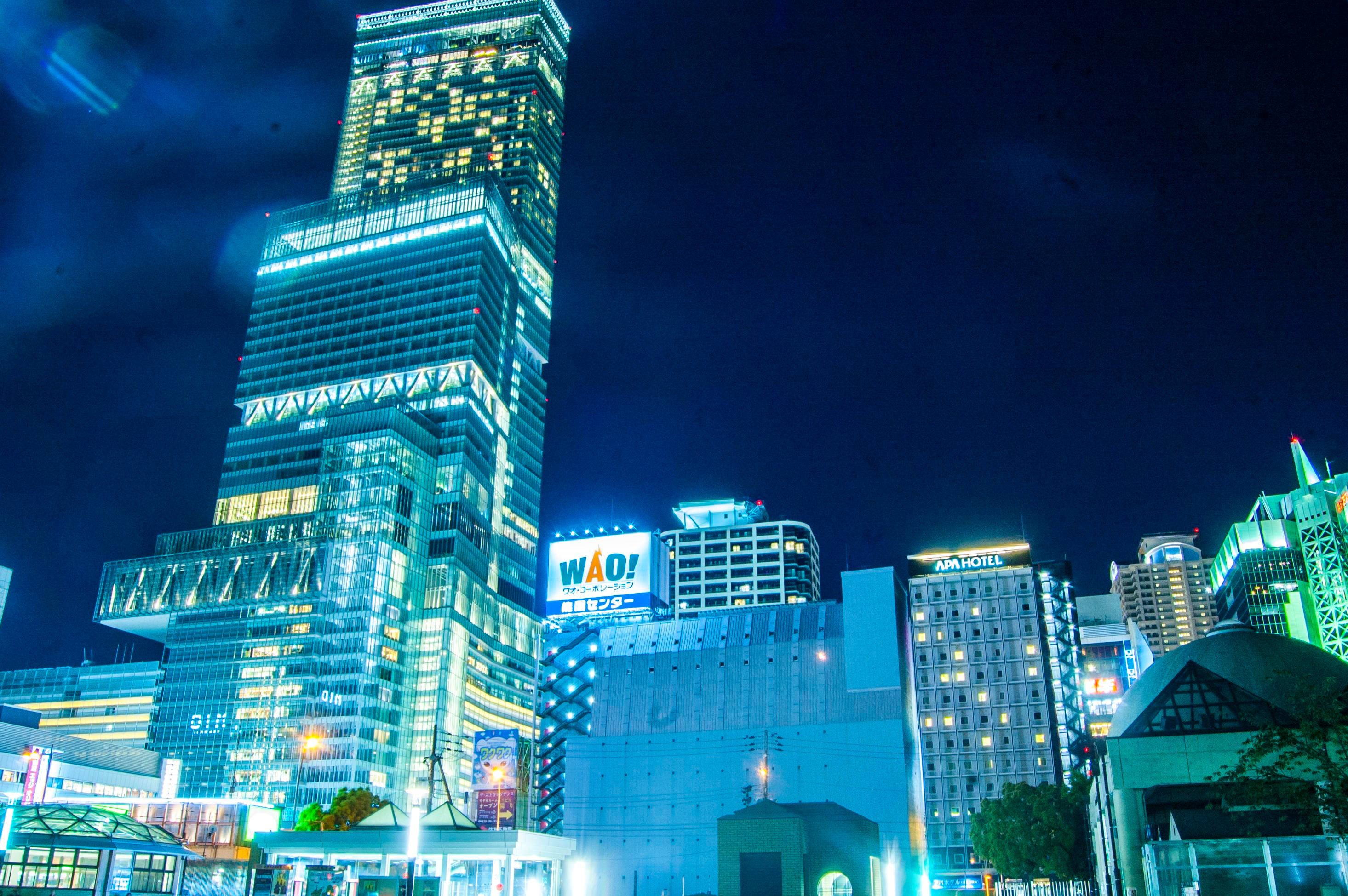 大阪最高建築夜景 壁紙 — 一座高聳的摩天大樓在繁華的城市天際線中，在黑暗的夜空下閃耀著藍色和白色的燈光。