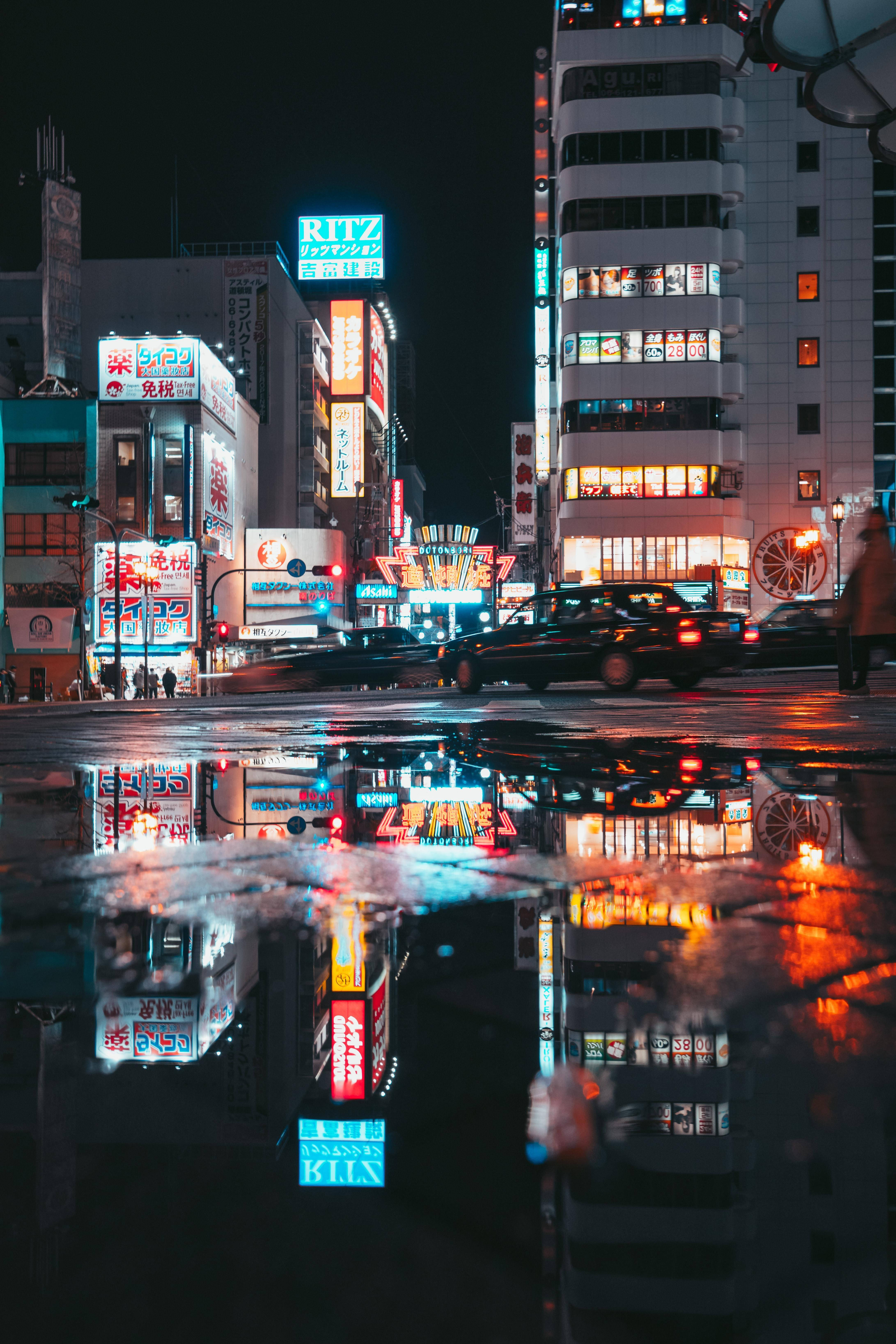 大阪道頓堀夜景 壁紙 — 雨濕的東京夜晚街道，在閃亮的水坑中反射出霓虹燈和移動的汽車。