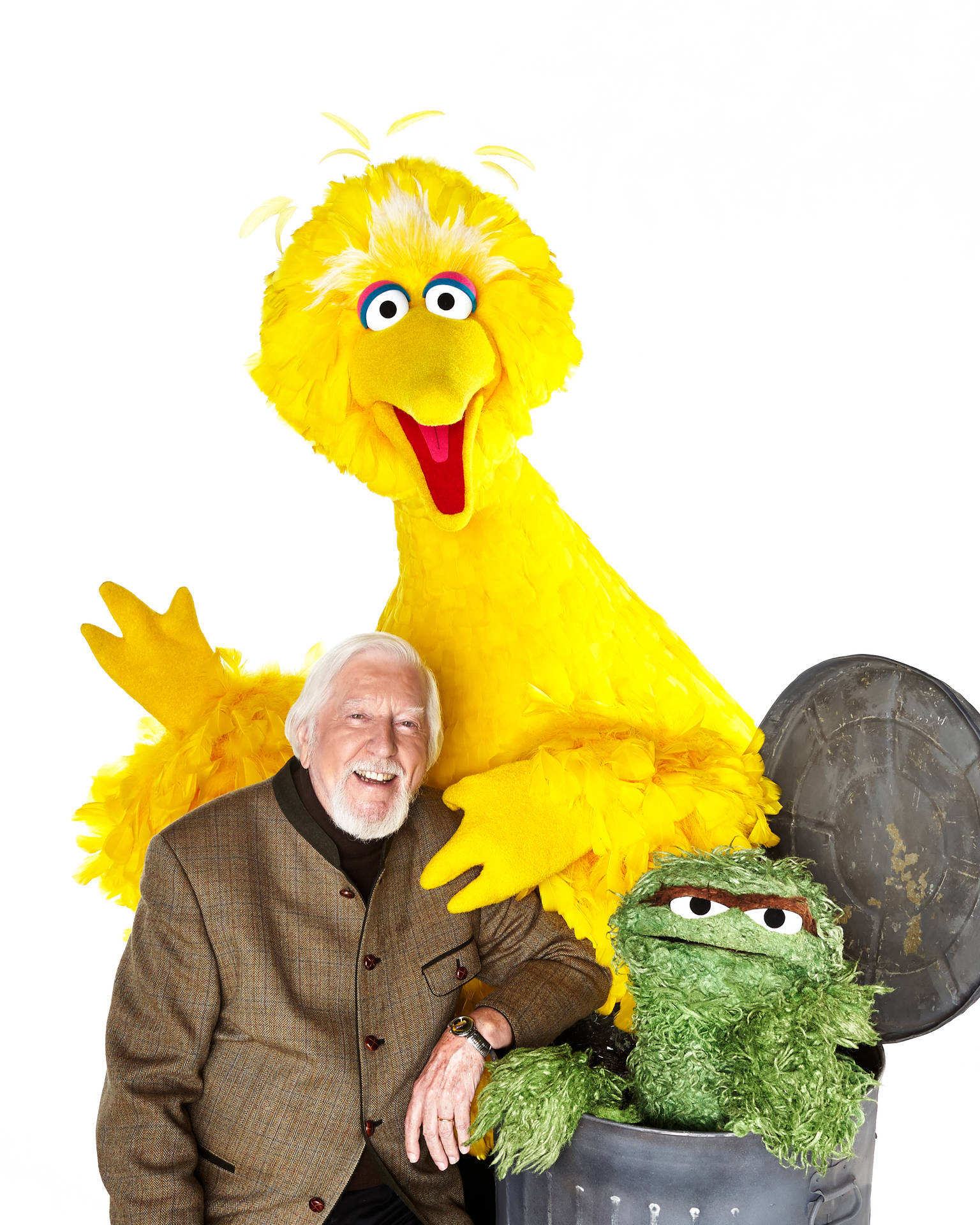 一個開心嘅男人同 Big Bird 同 Oscar the Grouch 喺白色背景前擺甫士。