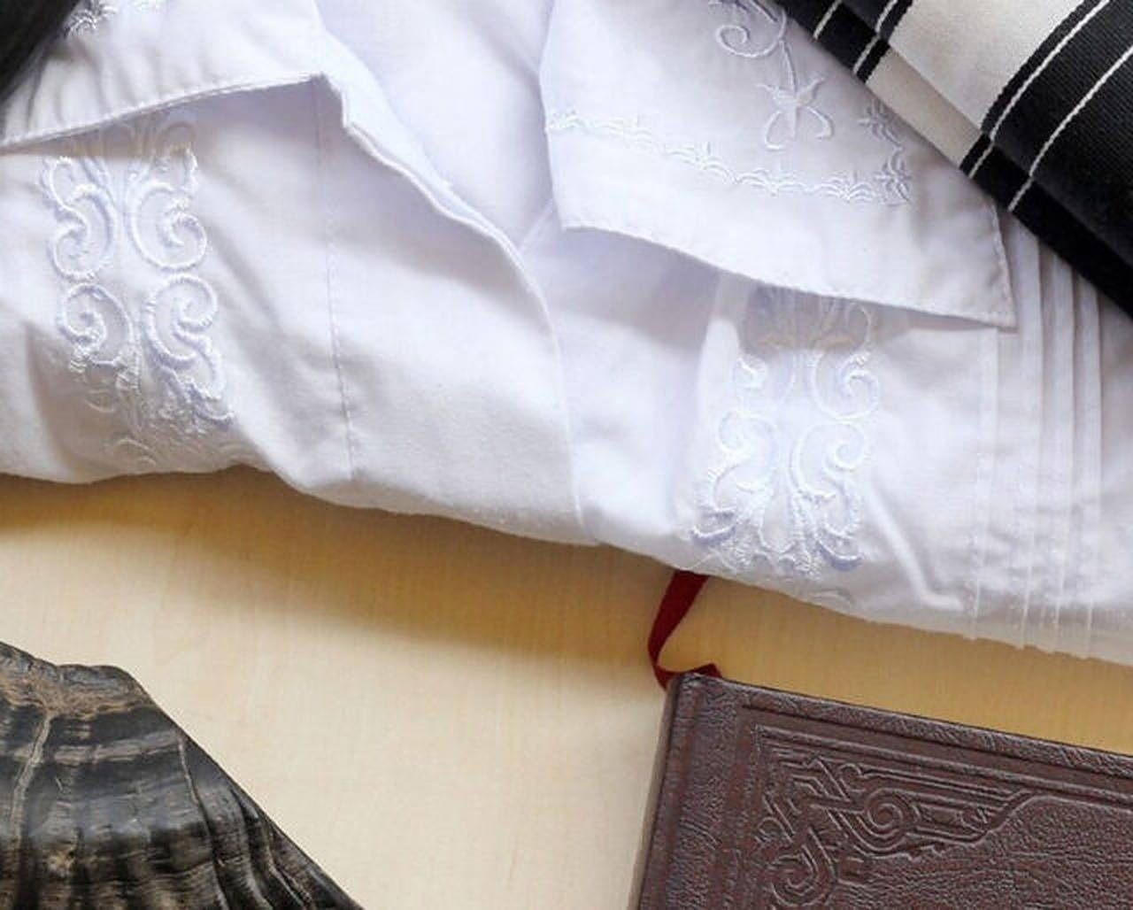 大齋節服飾 壁紙 — 淺色木頭上白色刺繡床單、黑色條紋布料及棕色皮面書本的近距離特寫。