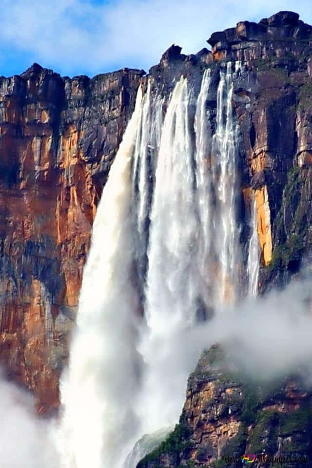 天使瀑布的風景 壁紙 — 巨大的瀑布從崎嶇的懸崖面傾瀉而下，在藍天下形成霧狀水花。