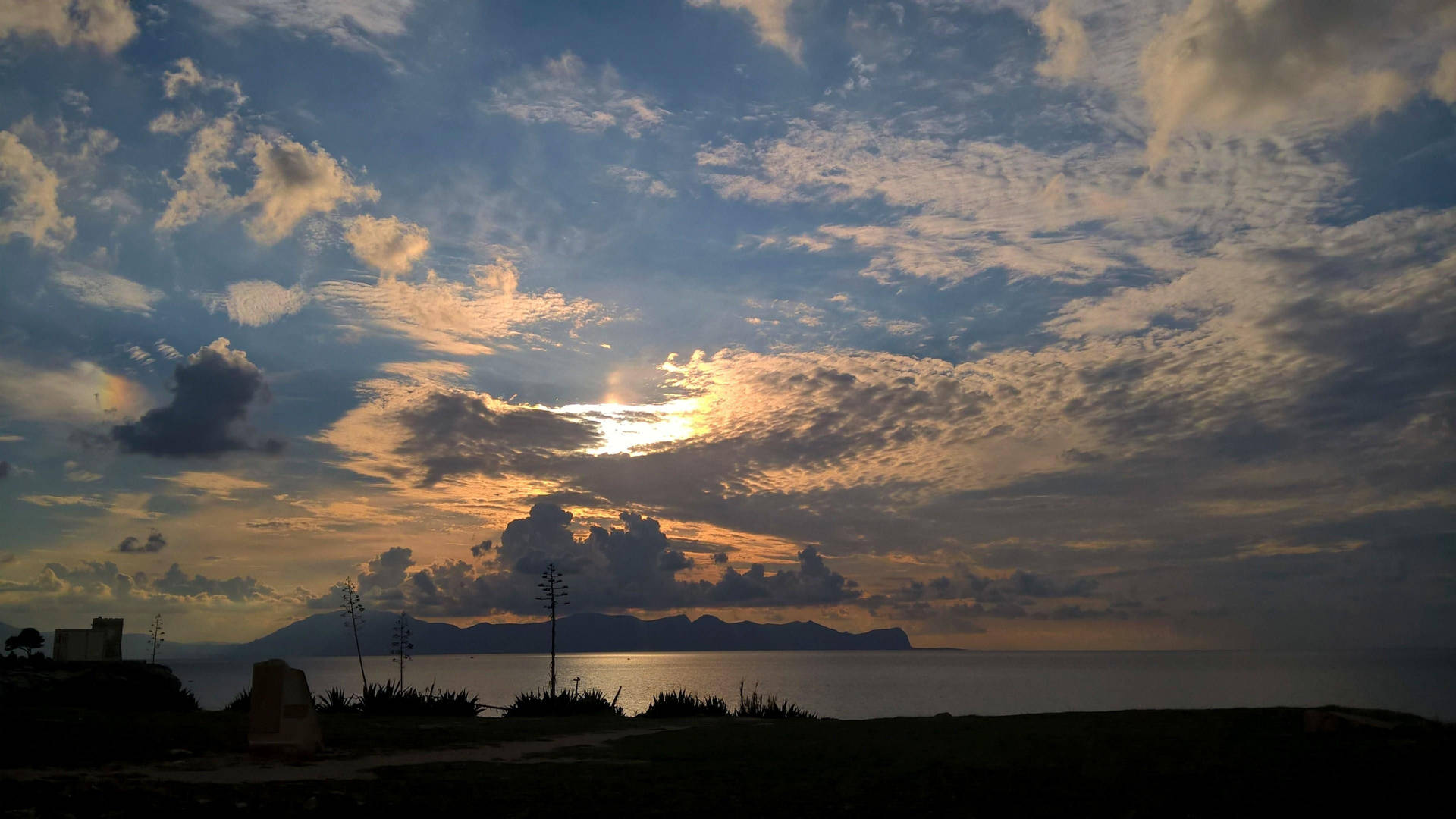 海洋上的夕陽，山巒輪廓和散落的雲彩。