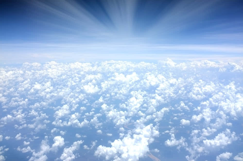 「天堂的壯麗風景」 壁紙 — 從高空俯瞰蓬鬆的白雲在燦爛的藍天下延伸，陽光從上方迸發而出。