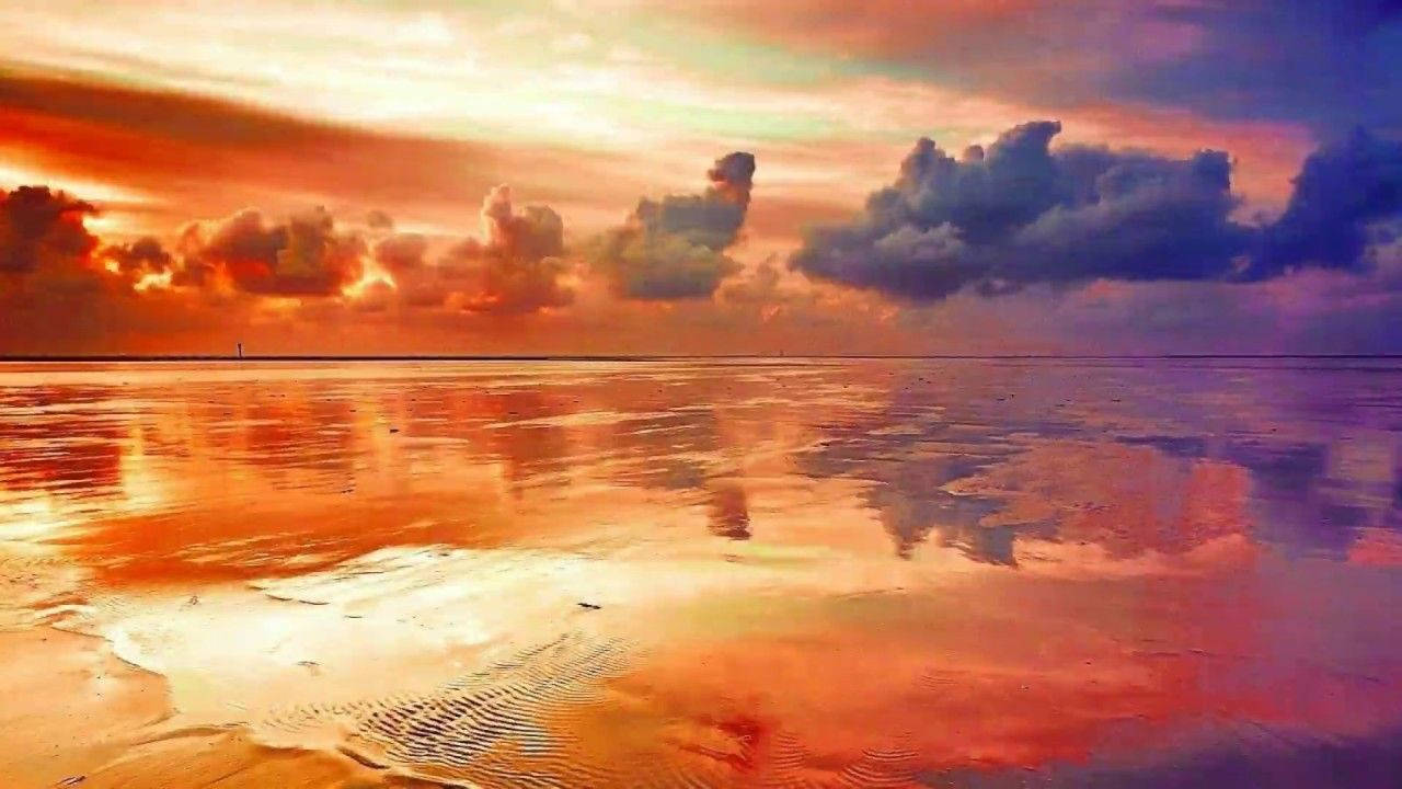 海灘上的日落，鮮豔的橙色和紫色雲彩映照在濕沙上。