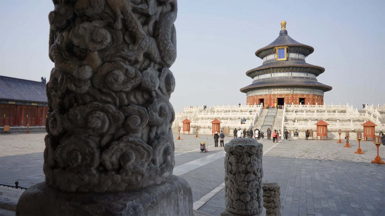 天壇帝壇柱基 壁紙 — 一座宏偉的傳統中式寺廟，擁有分層的藍色屋頂，矗立在雕刻精美的石柱後面，天空晴朗。