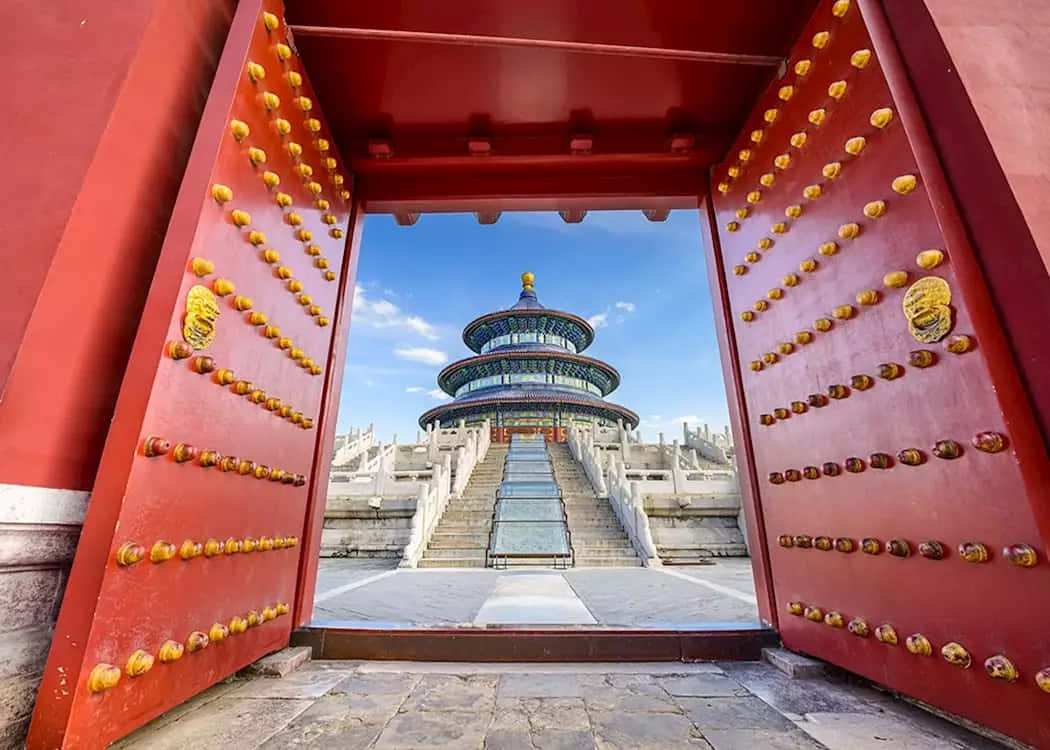 天壇皇穹宇門外的祈年殿 壁紙 — 一座帶有金色門釘的宏偉紅色大門，在清澈的藍天下框住天壇。
