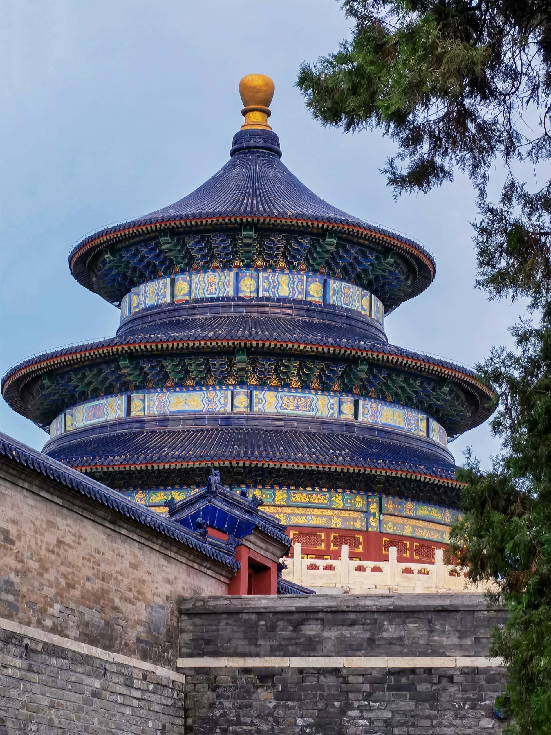 天壇祈穀殿的圓形建築 壁紙 — 一座宏偉的藍色瓷磚寺廟，帶有金色點綴，在晴朗的天空下聳立，周圍環繞著茂密的綠色樹木。