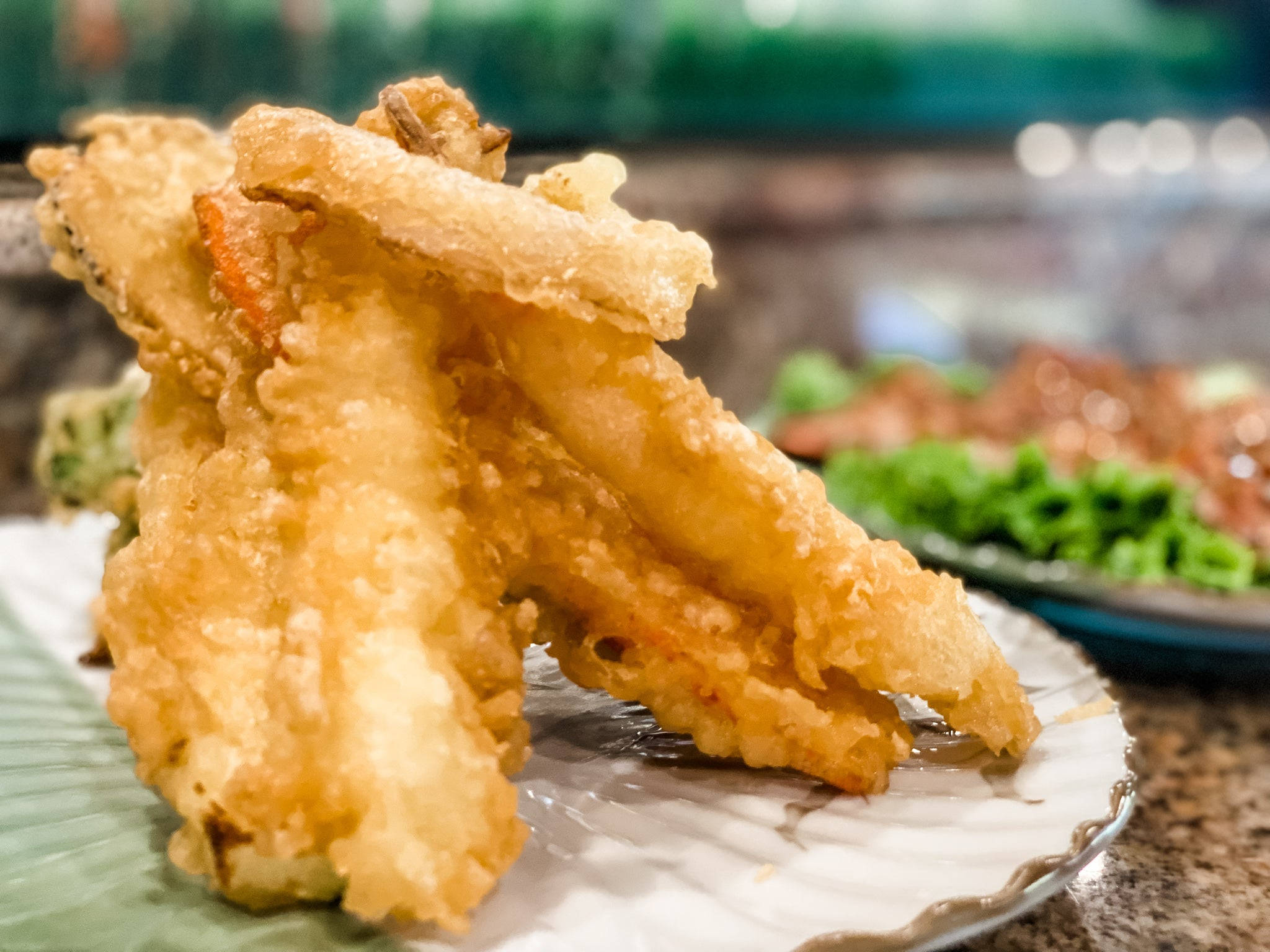 天婦羅與蔬菜套餐 壁紙 — 金黃酥脆的天婦羅蔬菜高高堆在白色盤子上，帶有模糊的綠色裝飾和背景。