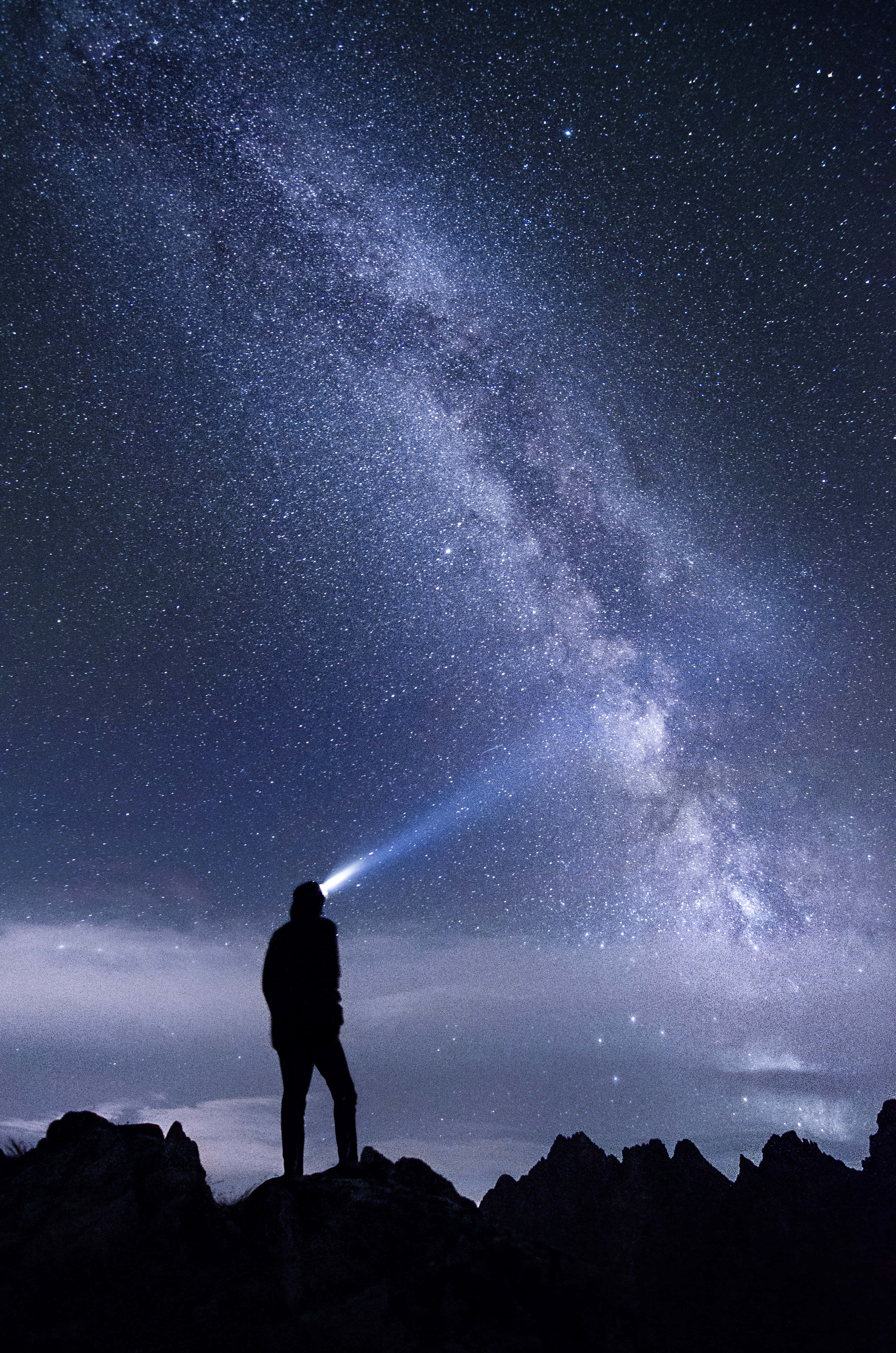 天文學家的光暈剪影 壁紙 — 夜晚，一個孤獨的身影站在岩石山頂上，將手電筒照向銀河系。