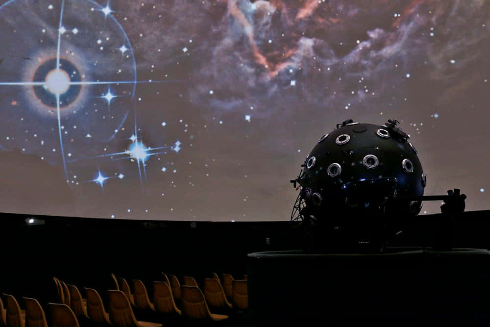 Planetarium 桌布 壁紙 — 天文館圓頂將充滿活力的星場和星雲投射到空座位上方嘅天花板上。