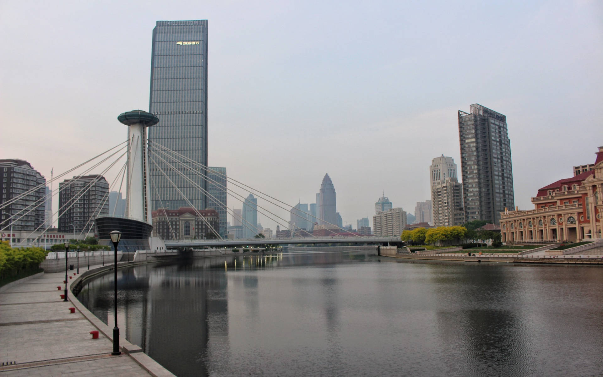 城市河流景觀，有斜拉橋和高樓大廈，天空多雲。