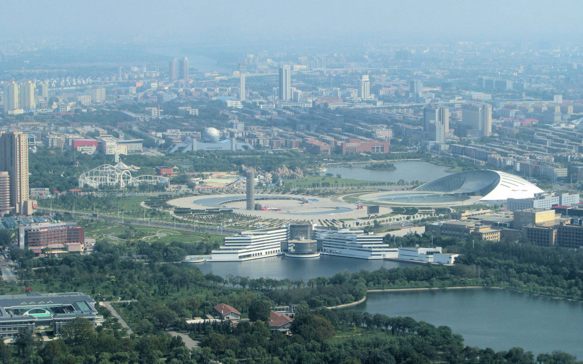 從高空俯瞰現代城市，有湖泊和綠地，天空朦朧。