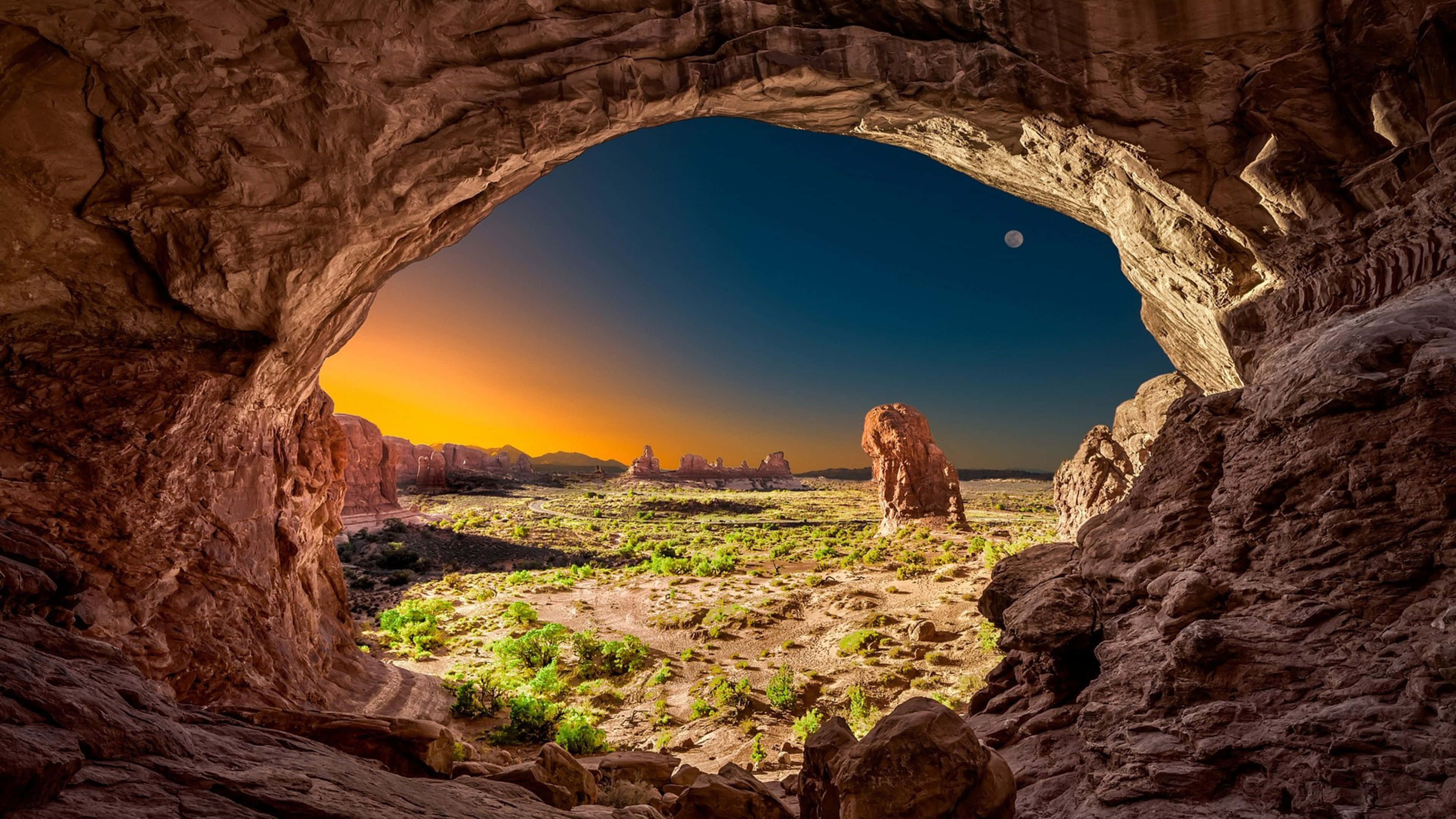4K Hdr 桌布 壁紙 — 天然石拱門框住日落時分的沙漠景色，遠方岩層上方有一彎新月。