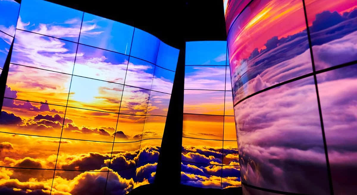 天空 OLED 圖 壁紙 — 彎曲的數碼屏幕在黑暗的房間中顯示雲層上充滿活力的日落。