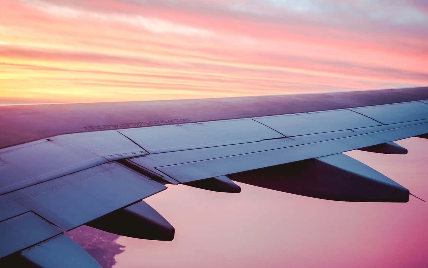 飛機機翼以海洋上方的粉紅色和橙色日落天空為背景。
