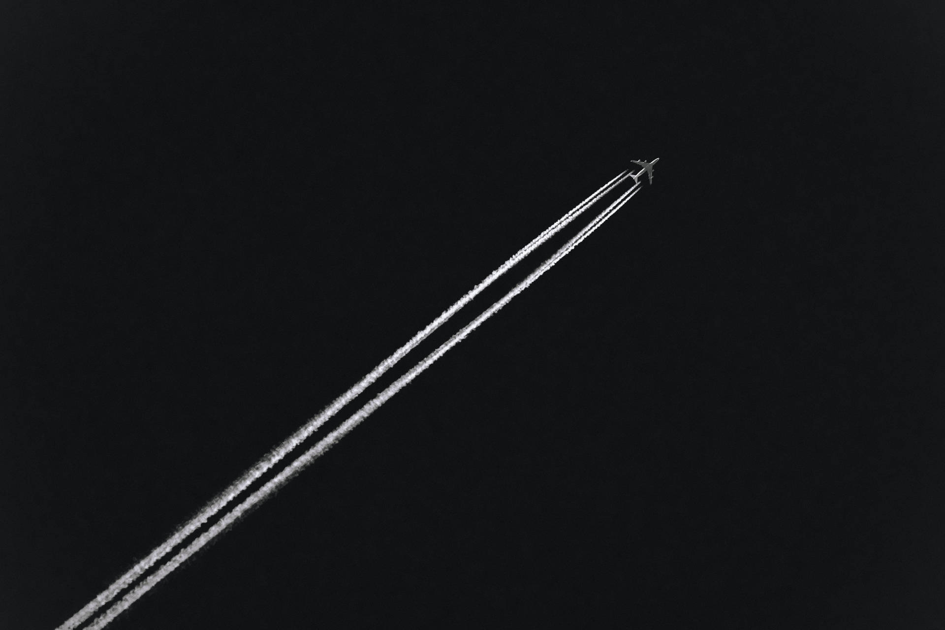 夜間飛行的飛機在黑暗的天空中留下兩條明亮的凝結尾跡。