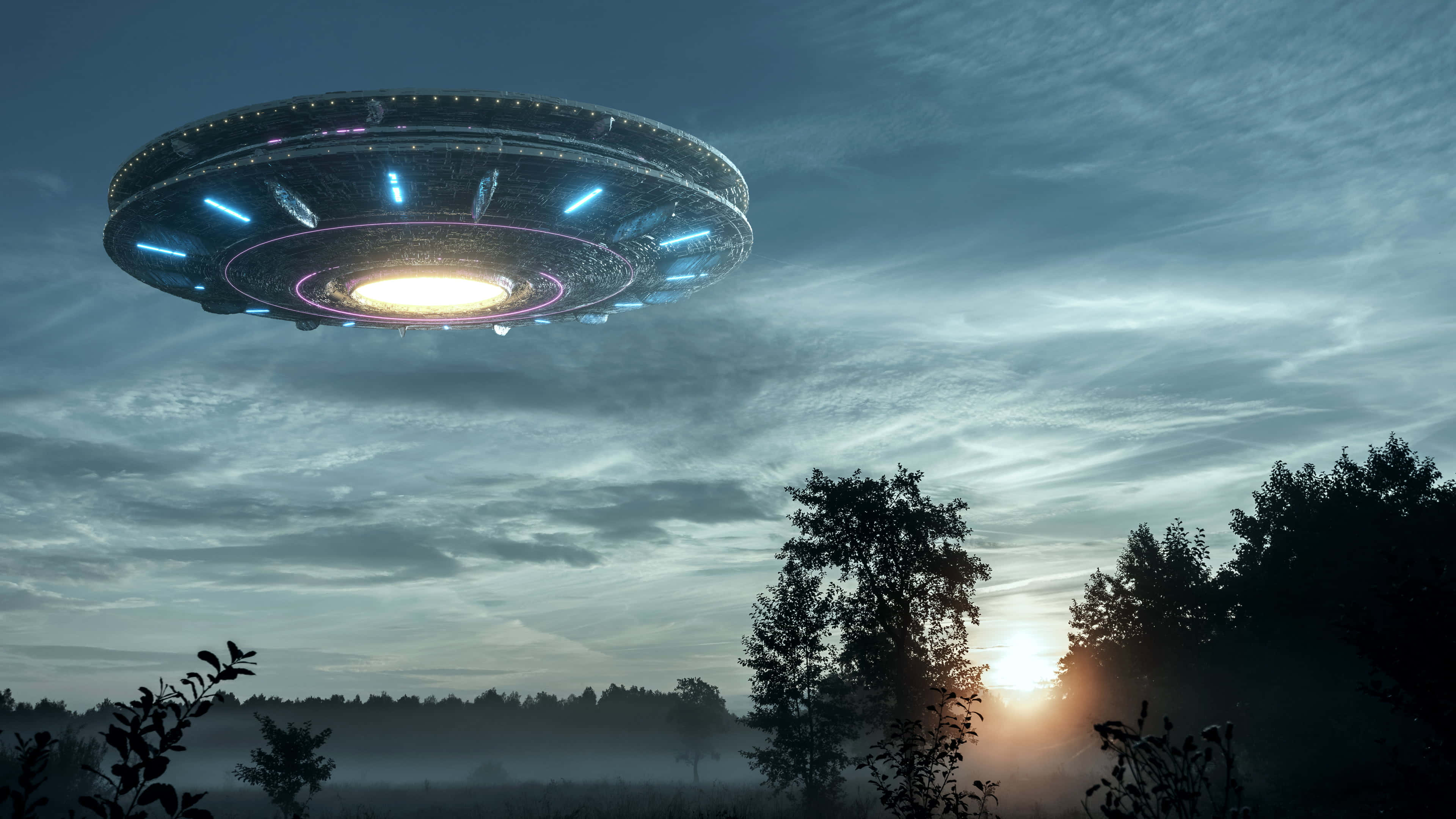 天空中發現：真實UFO 壁紙 — 一個發光的碟形UFO在日落時分懸浮在霧氣籠罩的森林上空，向多雲的天空投射出藍色和白色的光芒。
