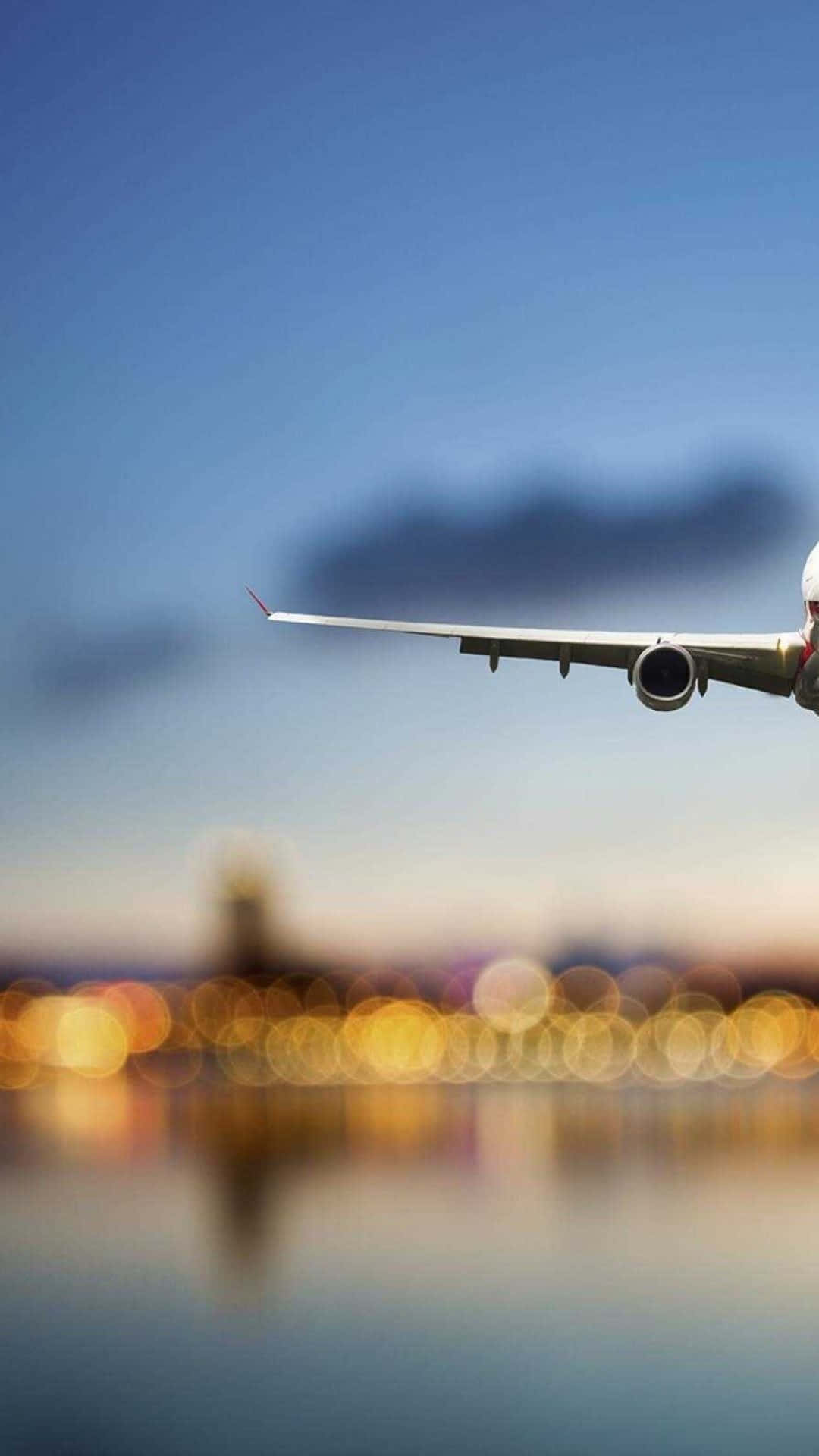 天空之美，飛機掠過雲層 壁紙 — 流線型飛機翼在晴朗藍天中滑翔，下方城市景觀閃爍著金色散景燈光。
