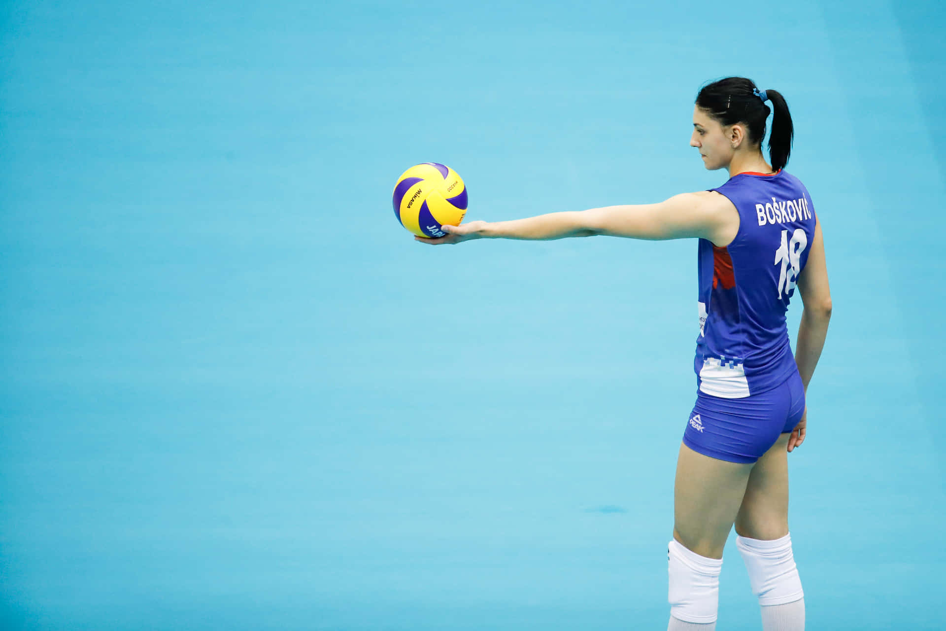 女排球運動員在藍色球場上發球。