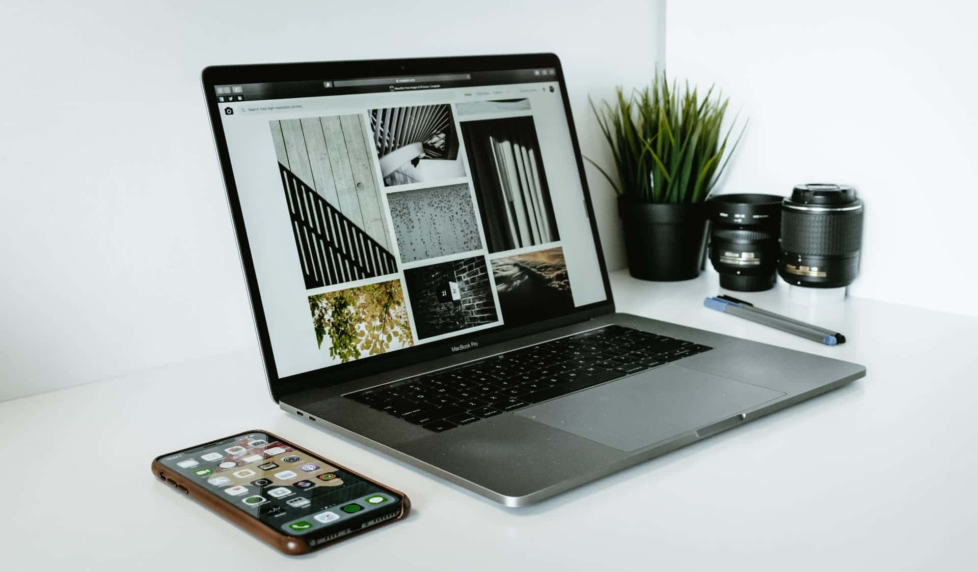 現代工作空間，配有筆記型電腦、手機、相機鏡頭和植物在白色桌子上
