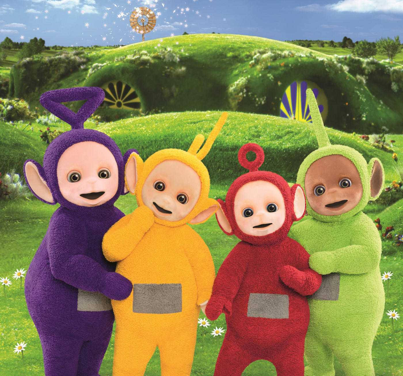 天線寶寶在天線寶寶樂園擺姿 壁紙 — 四個色彩繽紛的Teletubbies微笑著站在充滿活力的綠色草地上，身後有一座奇特的丘陵小屋。