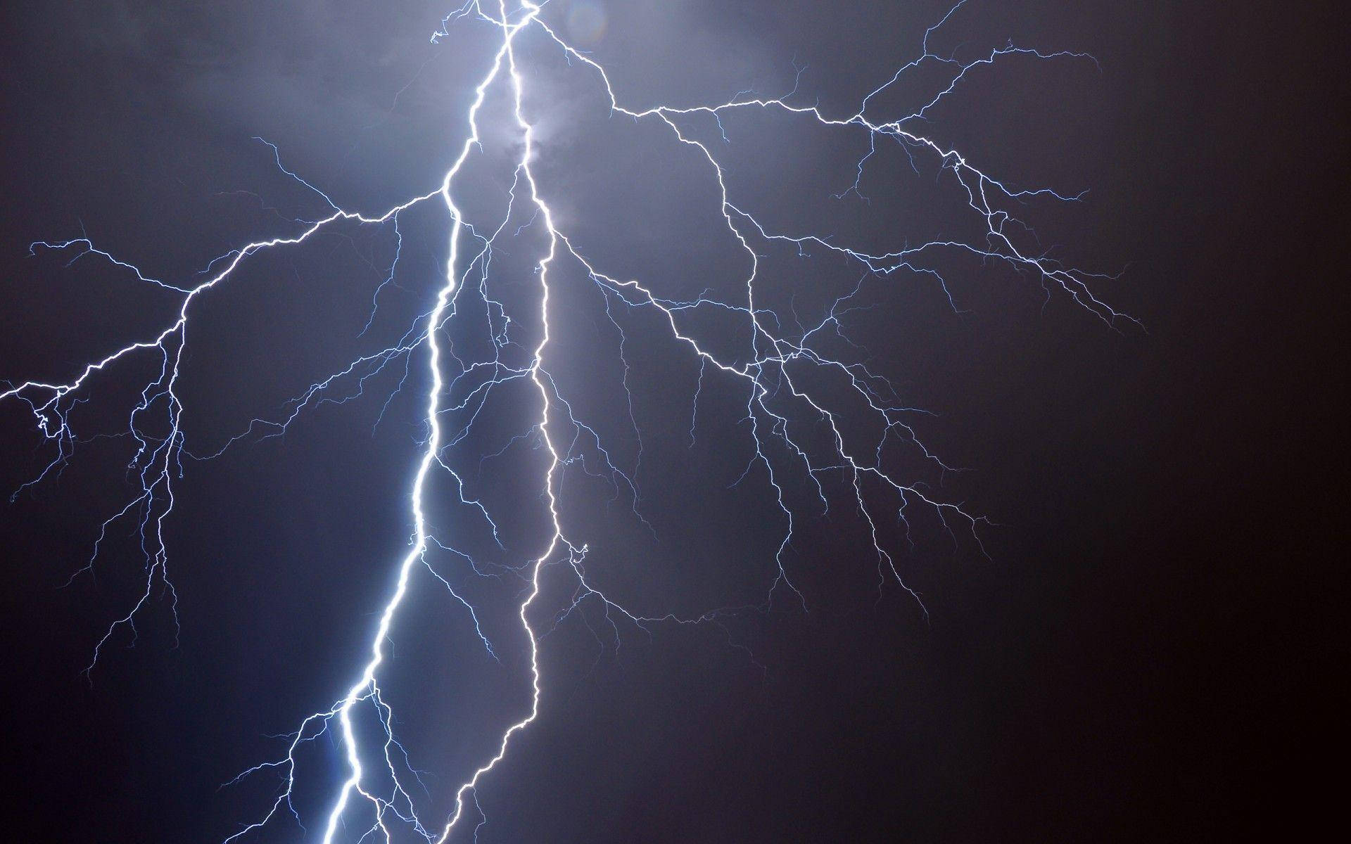 天降電光 壁紙 — 一道強大的閃電在黑暗的暴風雨天空中分叉，鋸齒狀的藍白色枝條照亮了雲層。