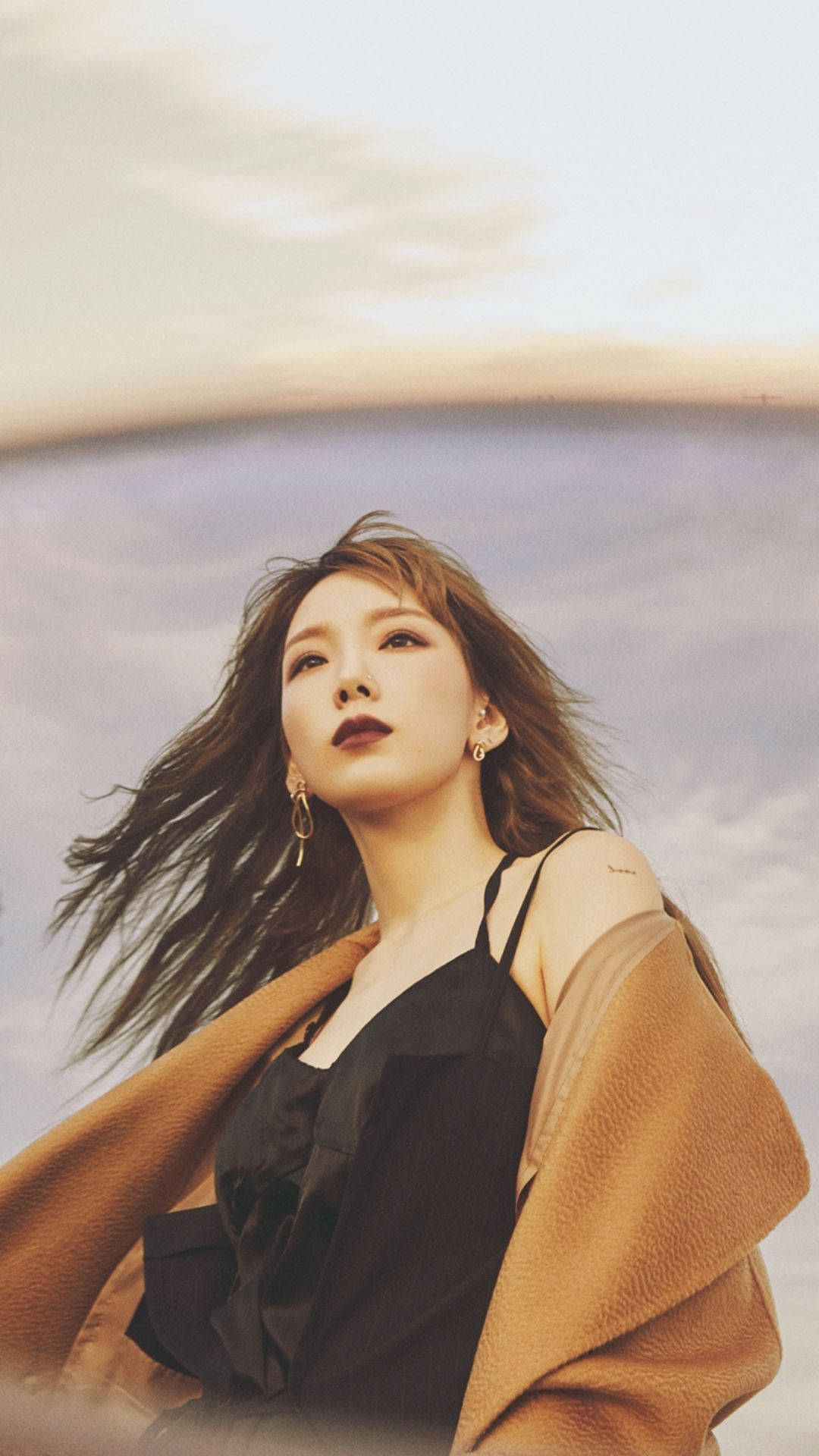太妍時尚風采 壁紙 — 一位頭髮被風吹拂的女性，在黃金時刻仰望柔和粉彩色的天空。