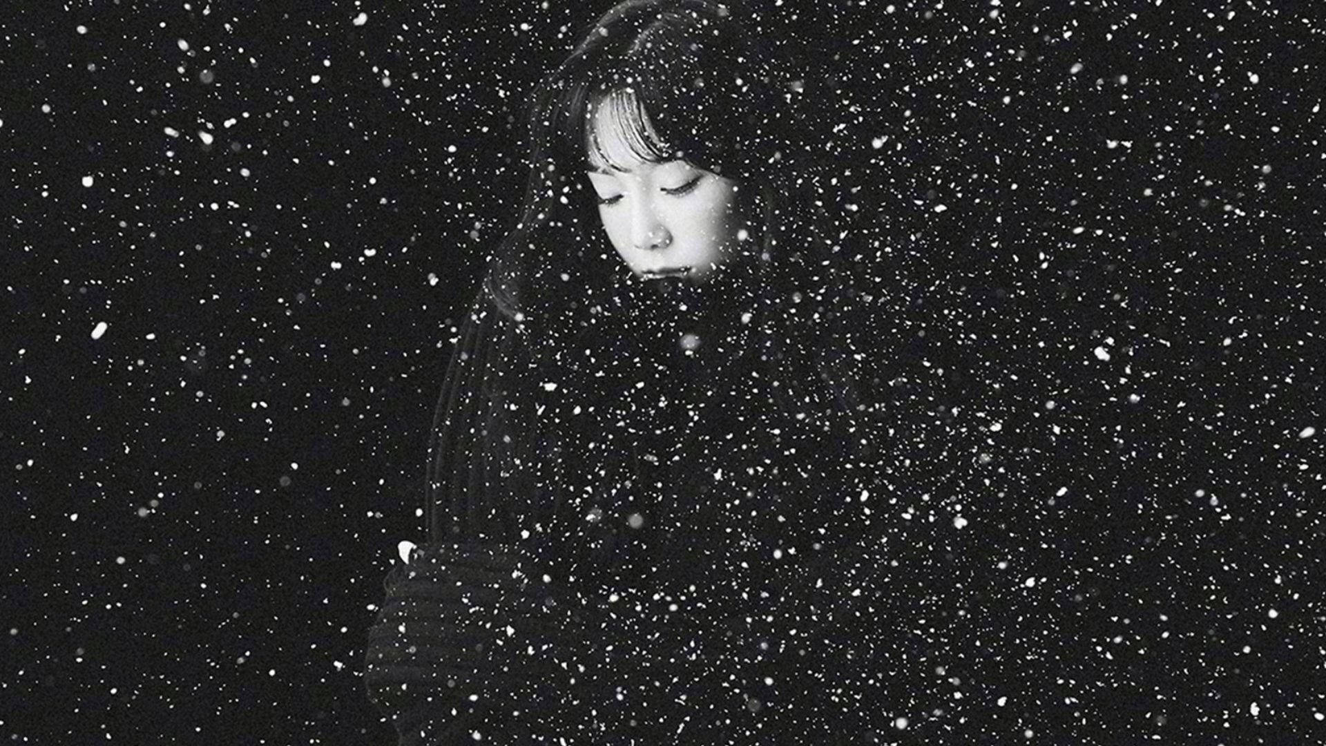 太妍與水花飛濺 壁紙 — 一位年輕女子閉著眼睛站在大雪中，她的臉在黑暗背景下被柔和地照亮。
