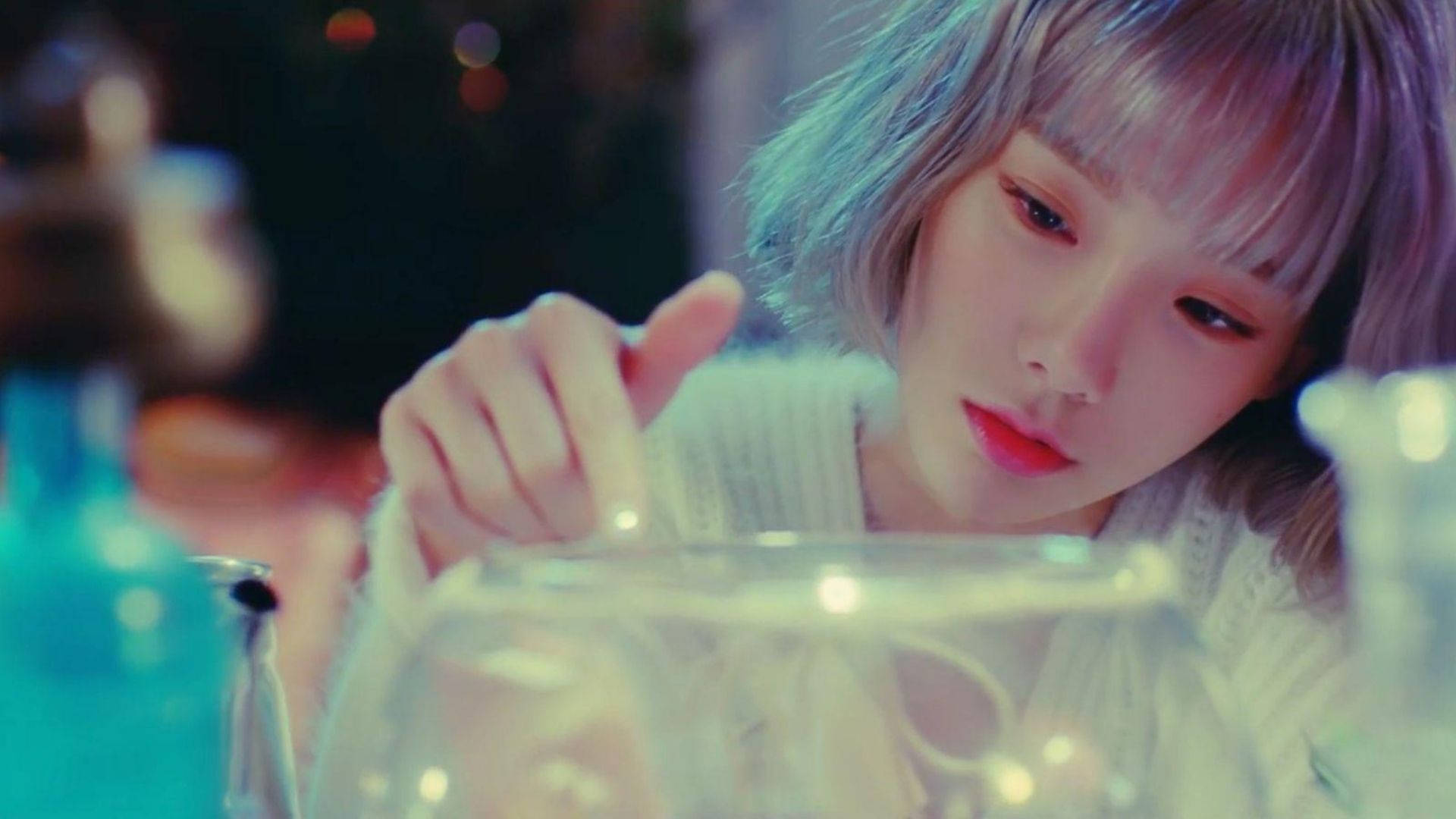 太妍觸碰脆弱魚缸 壁紙 — 一位年輕女性留著柔和色調的頭髮，在柔和光線且充滿散景的環境中俯身於玻璃碗上。