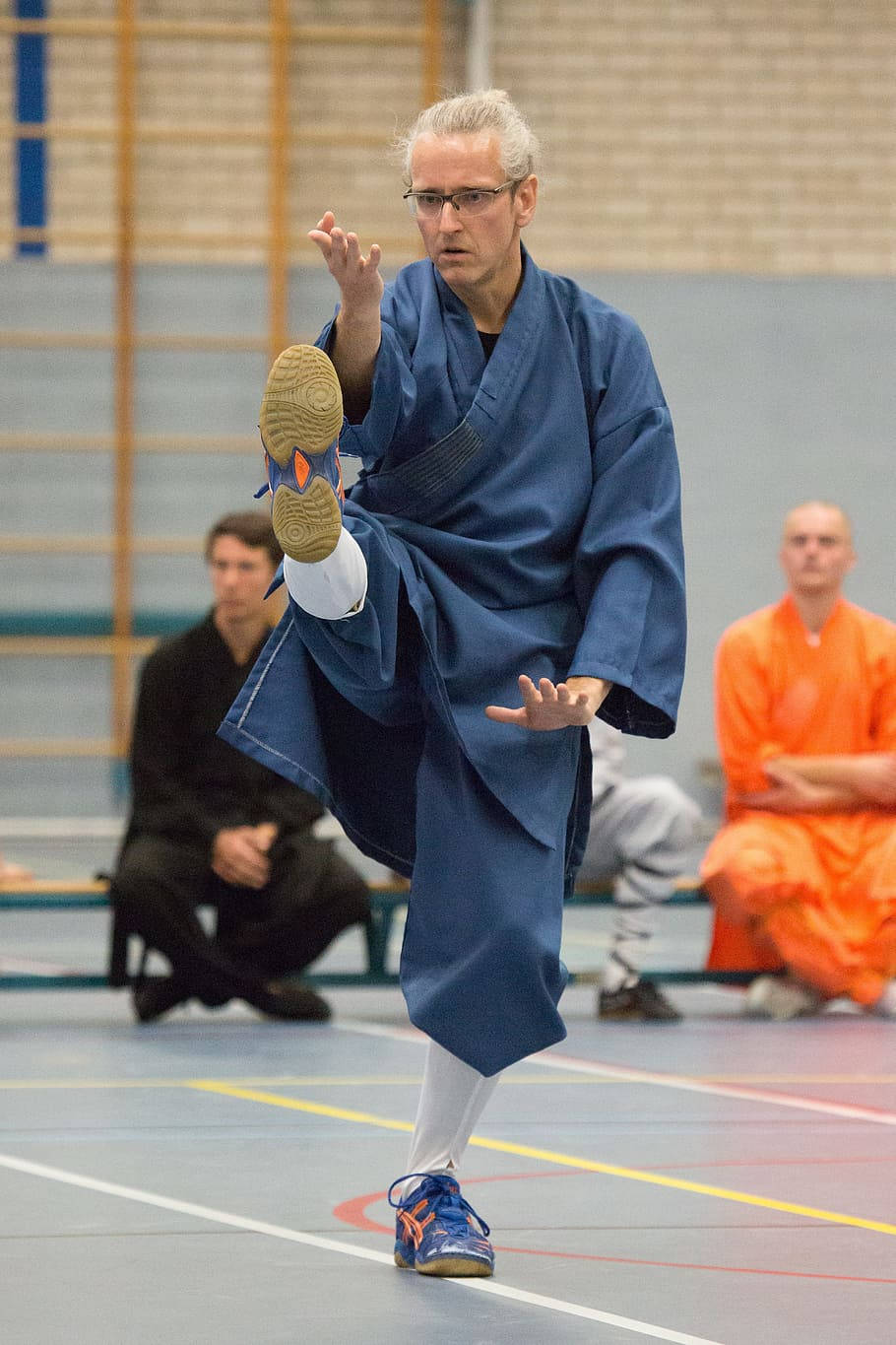 藍色道服男子在室內武術訓練中執行高踢。