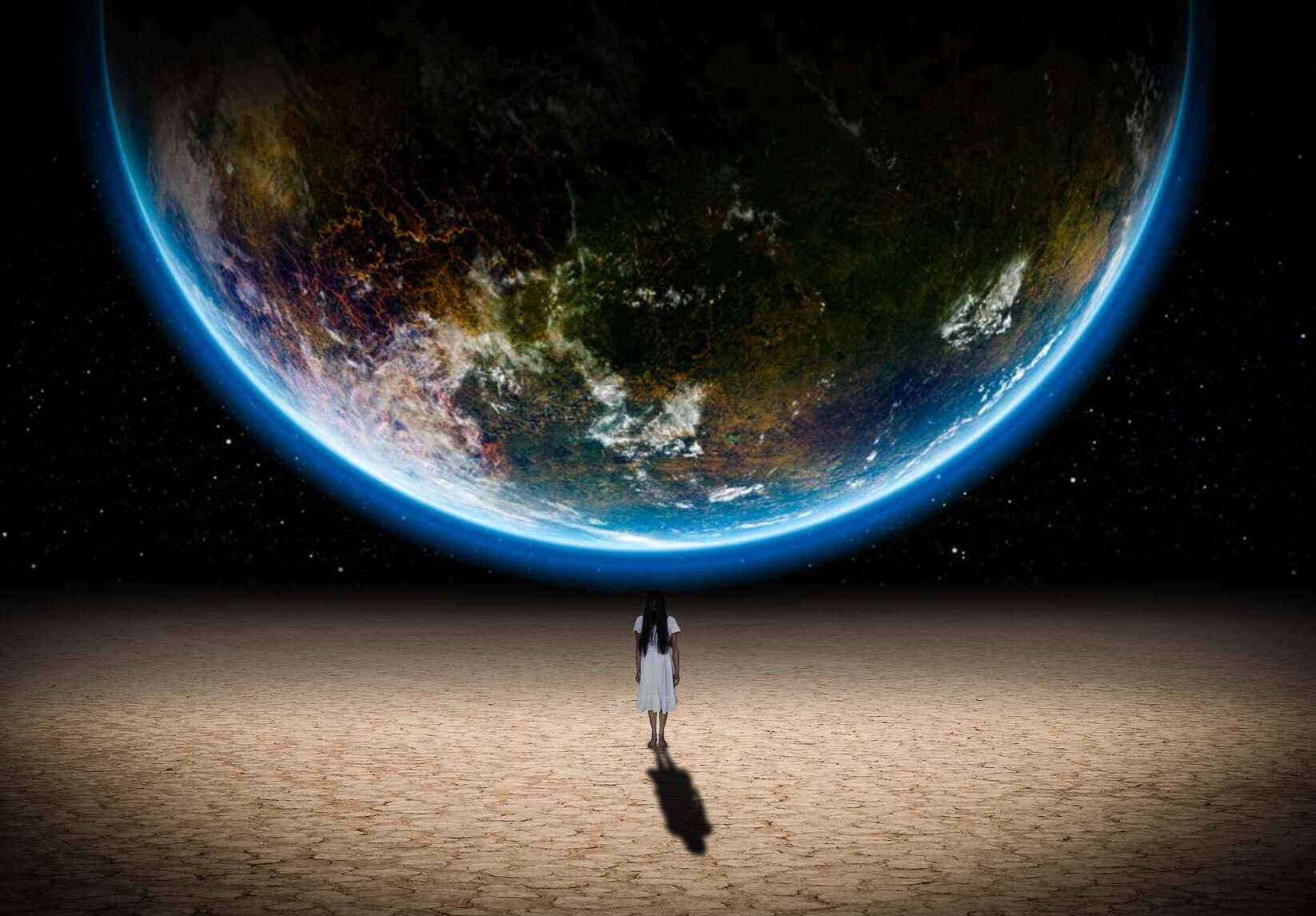 一個穿著白色連衣裙的人獨自站在沙漠星球上，看著太空中的地球。