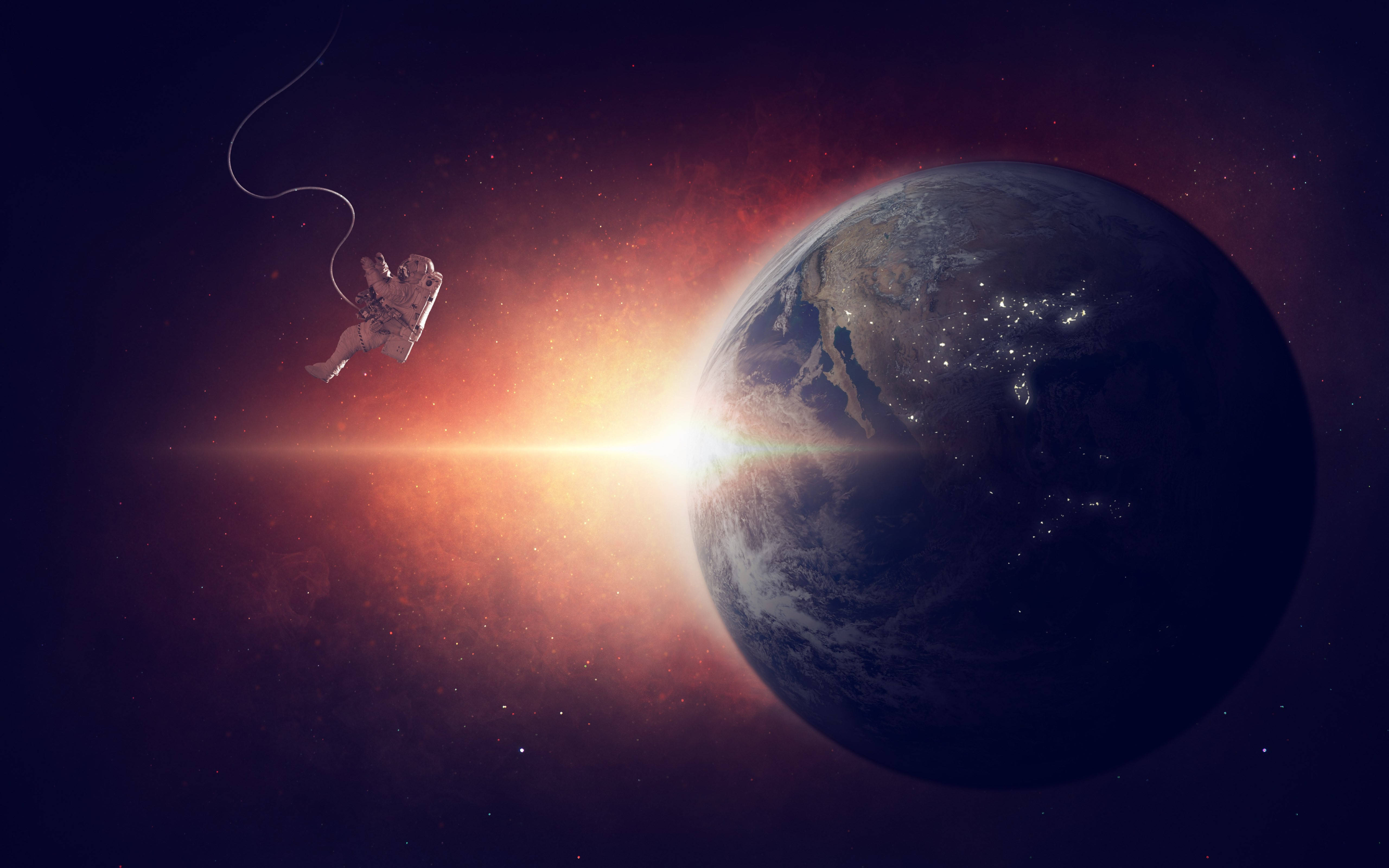 太空中的宇航員 壁紙 — 一名太空人漂浮在太空中，用纜繩繫在地球附近，地球因日出光線和城市燈光而發光。