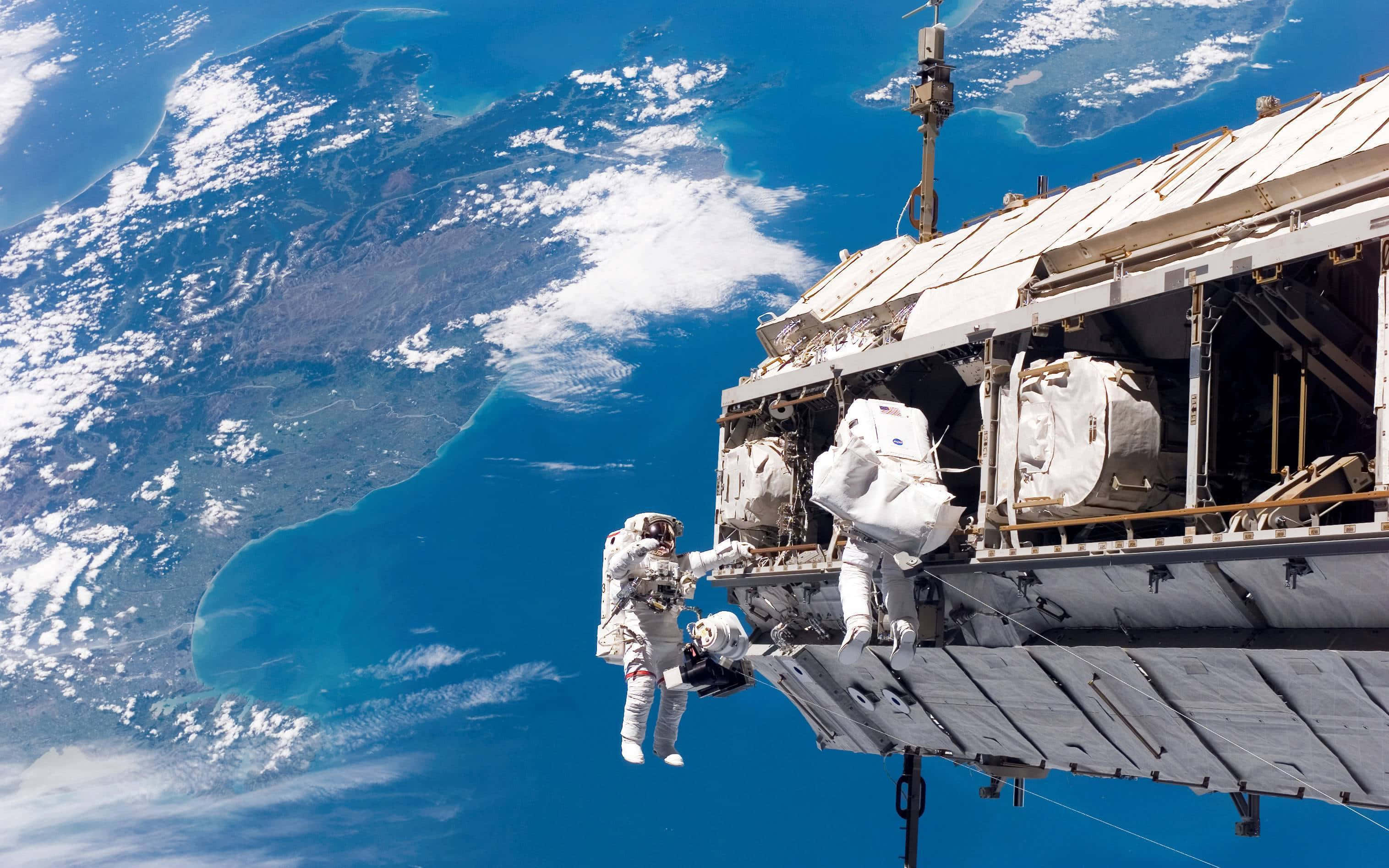 Iss 桌布 壁紙 — 太空人在國際太空站外進行太空漫步，下方可見地球的藍色海洋和白色雲層。