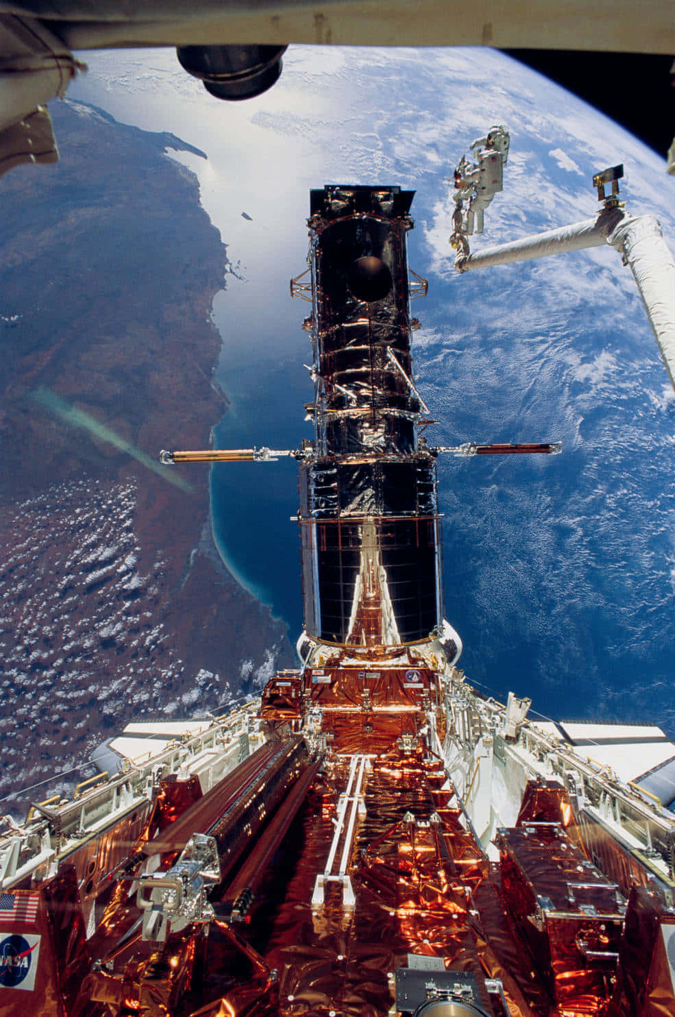 Hubble Space Telescope 桌布 壁紙 — 太空人在穿梭機的氣閘艙中，以地球的藍色海洋和棕色大陸為背景，修理哈勃太空望遠鏡。