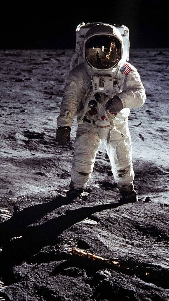 月球上的太空人穿著白色太空衣，地球在頭盔反射中可見。