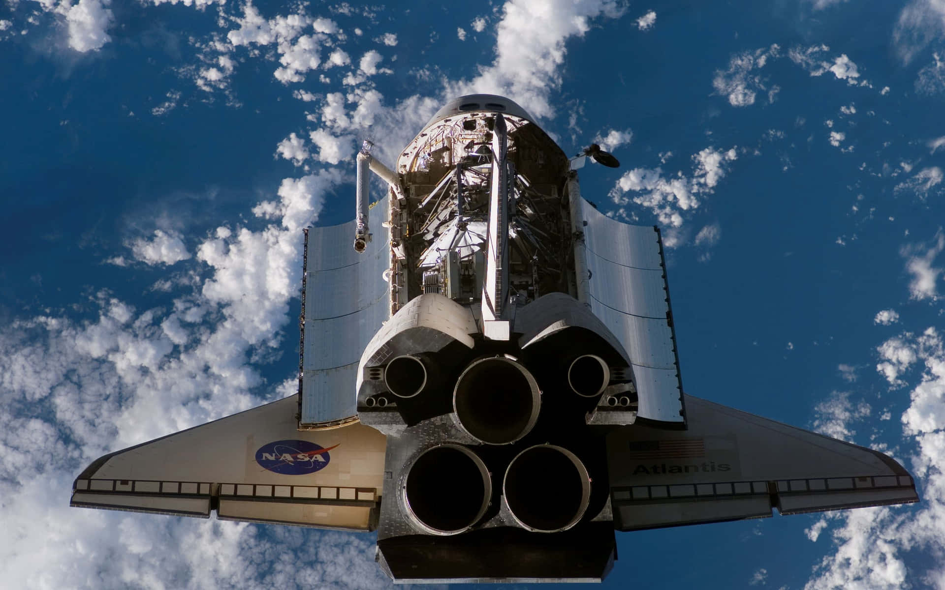 亞特蘭蒂斯號穿梭機在雲層上方飛行，NASA標誌清晰可見