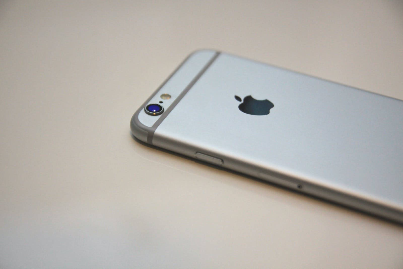 銀色 iPhone 6s 平放在純色表面上，顯示背面標誌和相機。