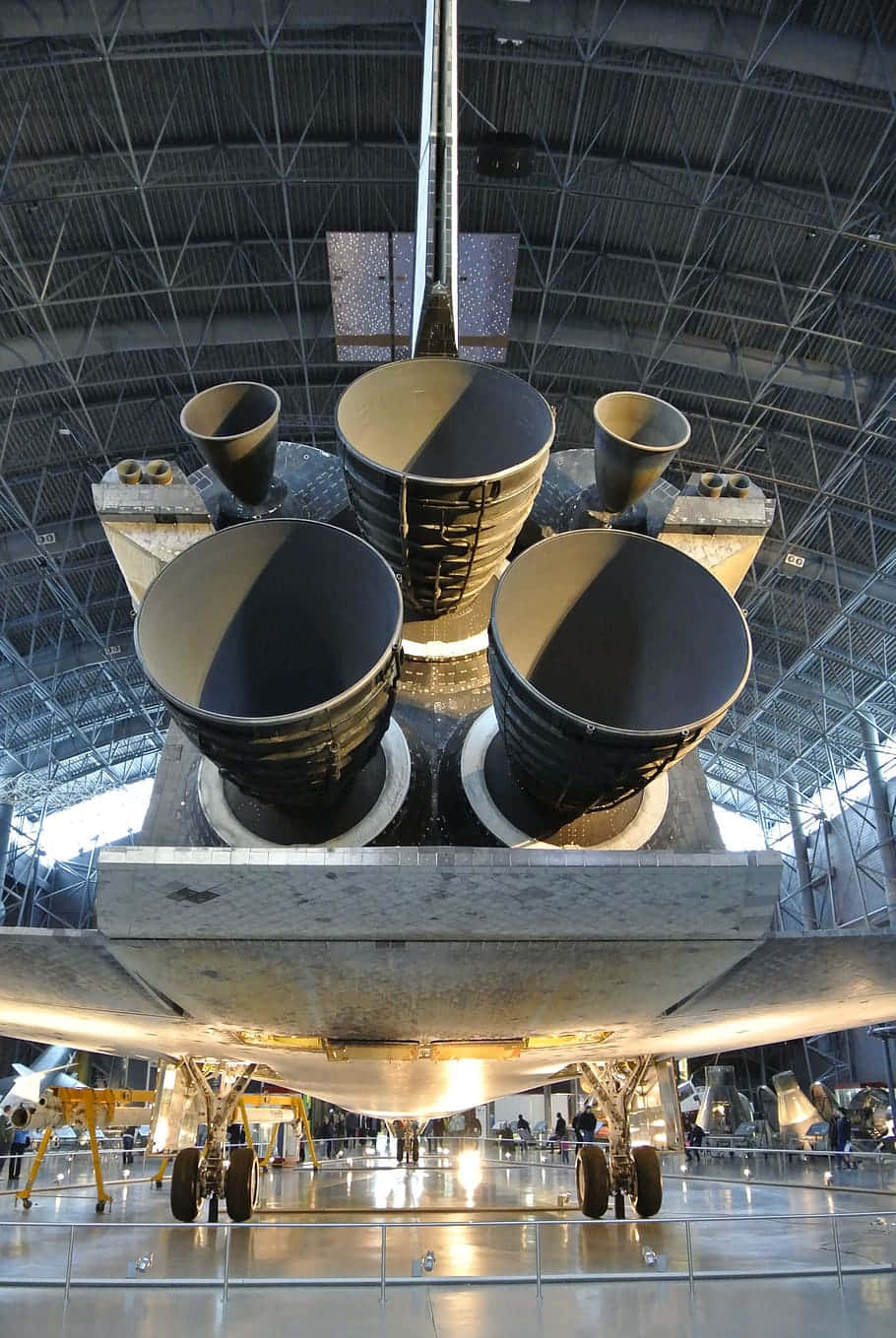 火箭 桌布 壁紙 — 太空穿梭機強力火箭引擎的近距離視圖，在廣闊的工業機庫內展出，下方有參觀者。