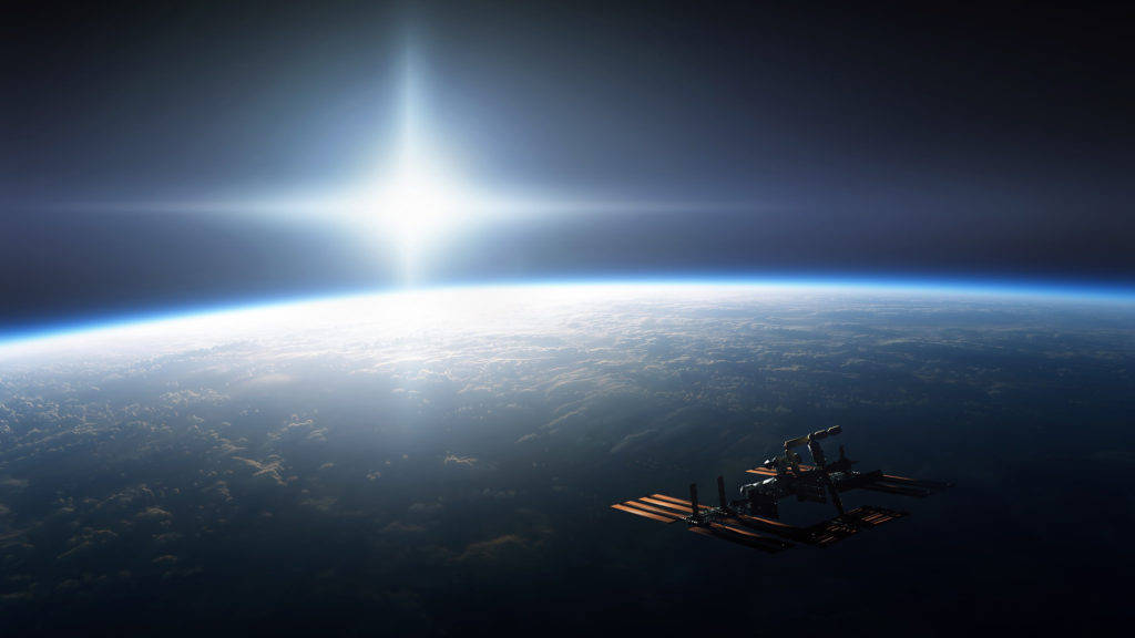 太空站環繞行星的電腦壁紙 壁紙 — 一個太空站繞著地球運行，太陽在行星彎曲的地平線上方明亮地照耀。
