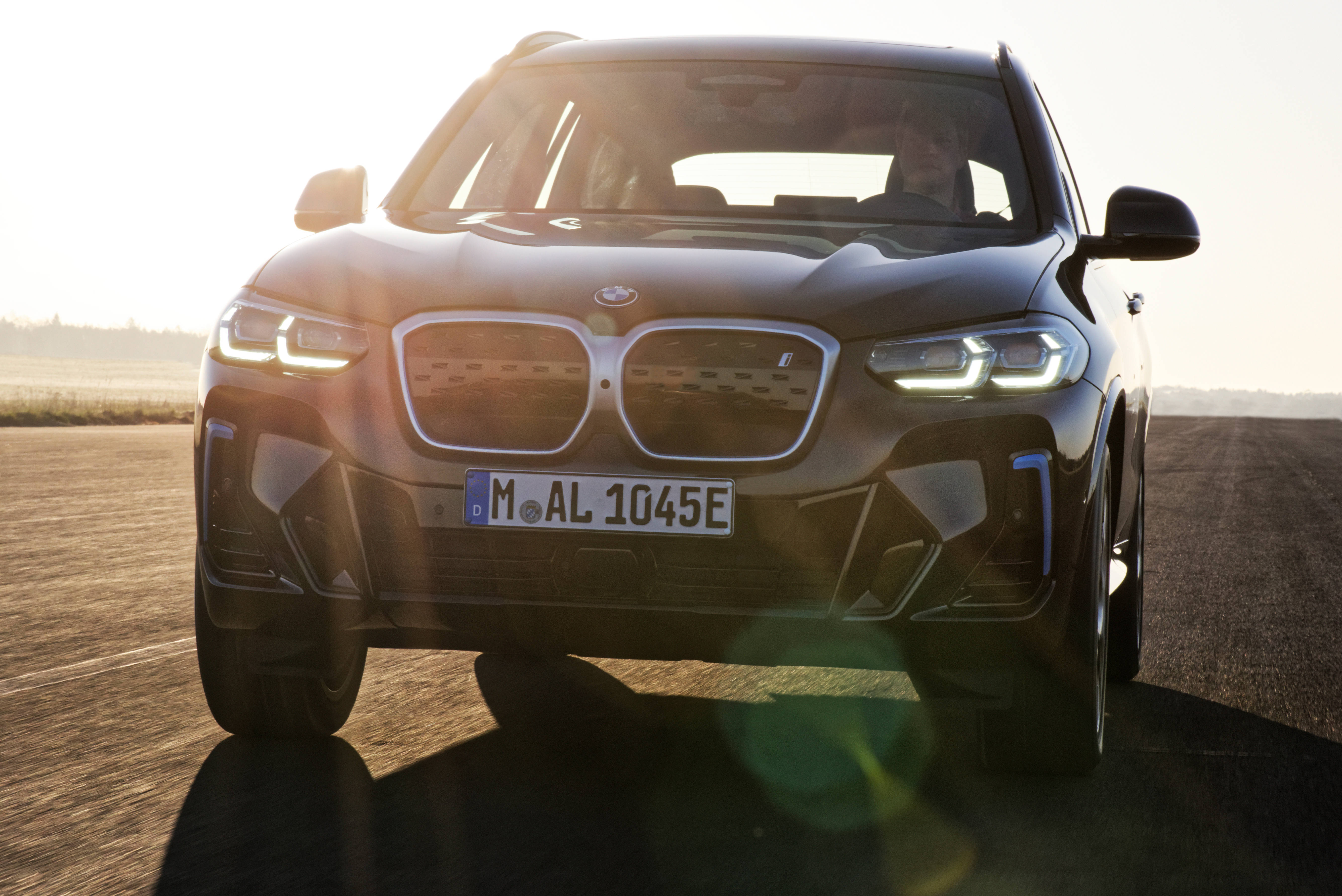太陽光暈下的黑色BMW 壁紙 — 一輛時尚的黑色BMW X3 SUV在陽光明媚的道路上向前行駛，車頭燈閃爍並帶有鏡頭光暈。