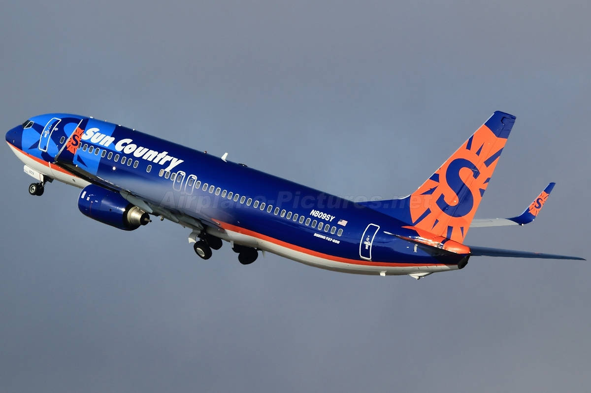Sun Country Airlines 飛機在灰色天空背景下放下起落架飛行。