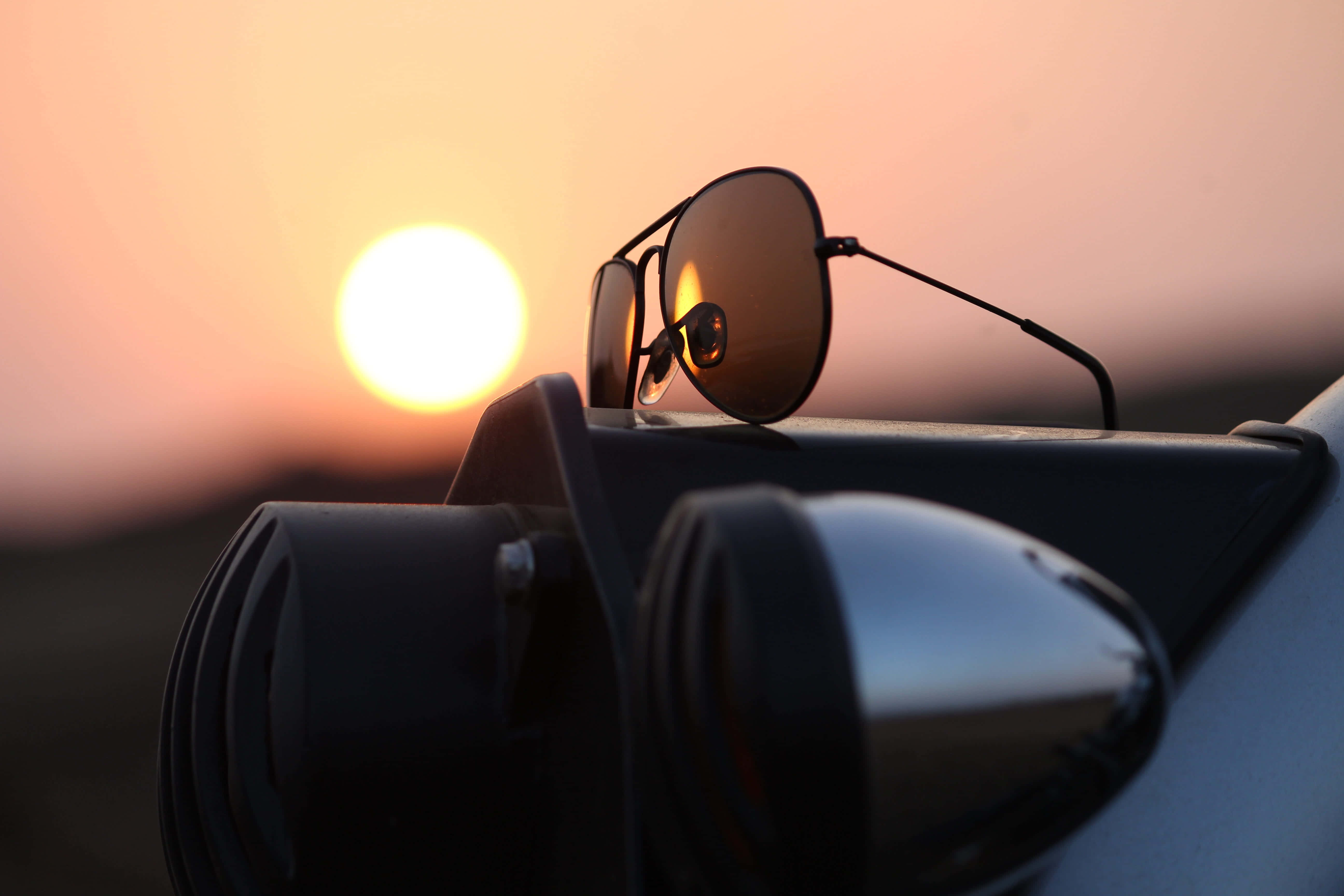 Sunglasses 桌布 壁紙 — 太陽眼鏡擱在汽車的側鏡上，夕陽在溫暖的橙色天空中落下。