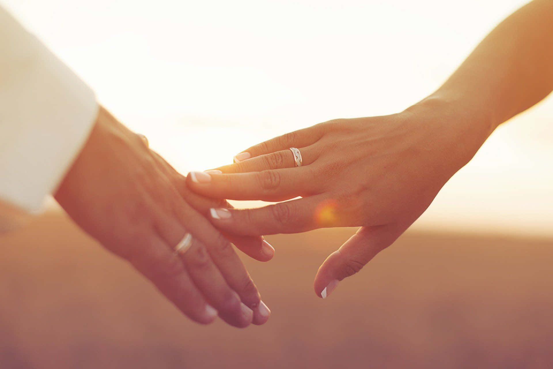 夫婦婚戒與夕陽 壁紙 — 兩隻手輕輕交握，結婚戒指在溫暖的金色夕陽光中閃耀。